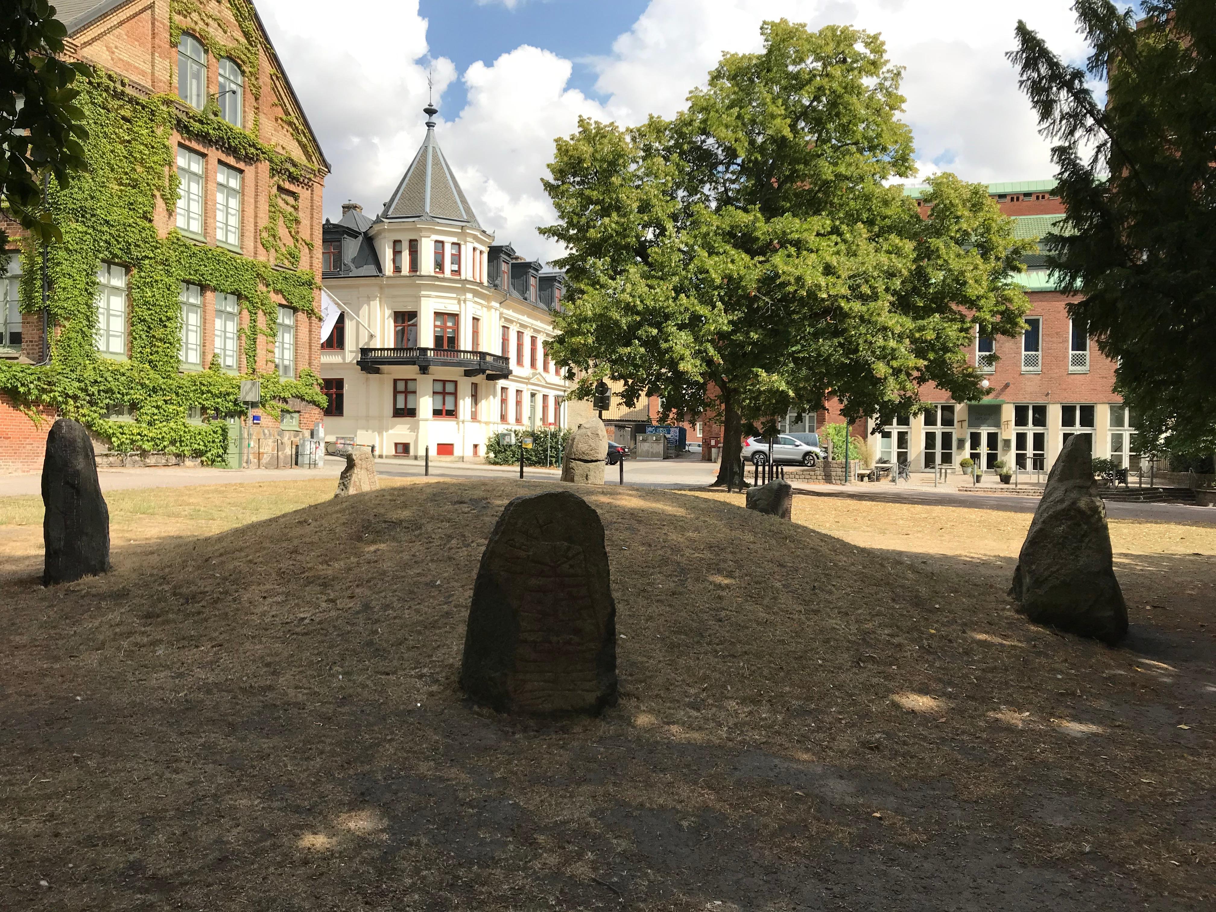 Carved standing stones on a grassy mound in front of old brick buildings