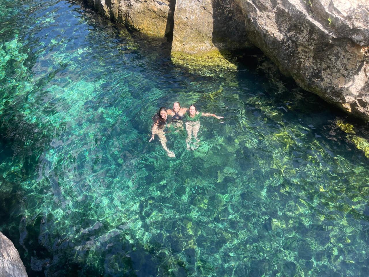 Three swimmers in clear cenote water seen from above