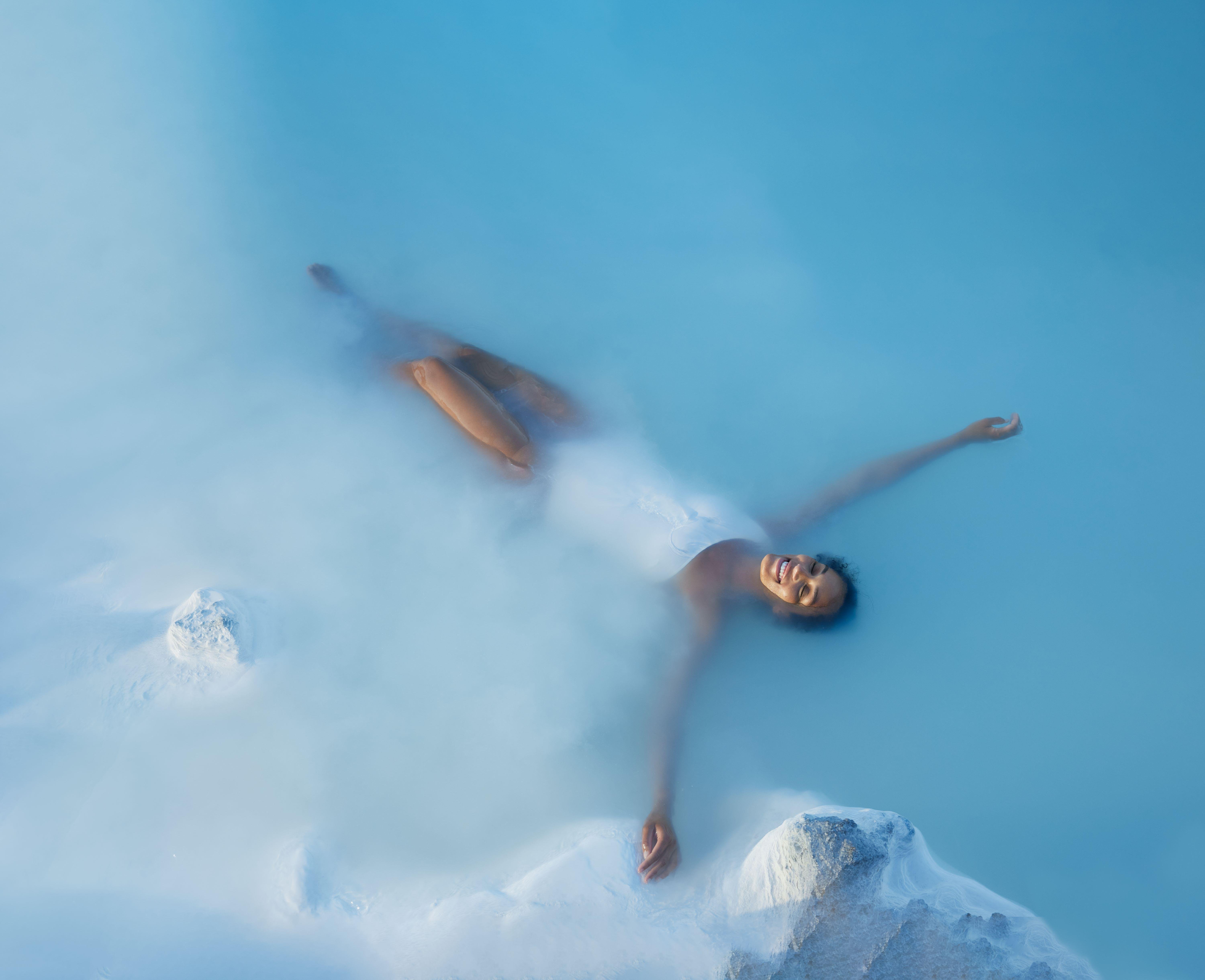 Visitor relaxing in the warm milky-blue Blue Lagoon water with a silica mud mask, Grindavik Iceland