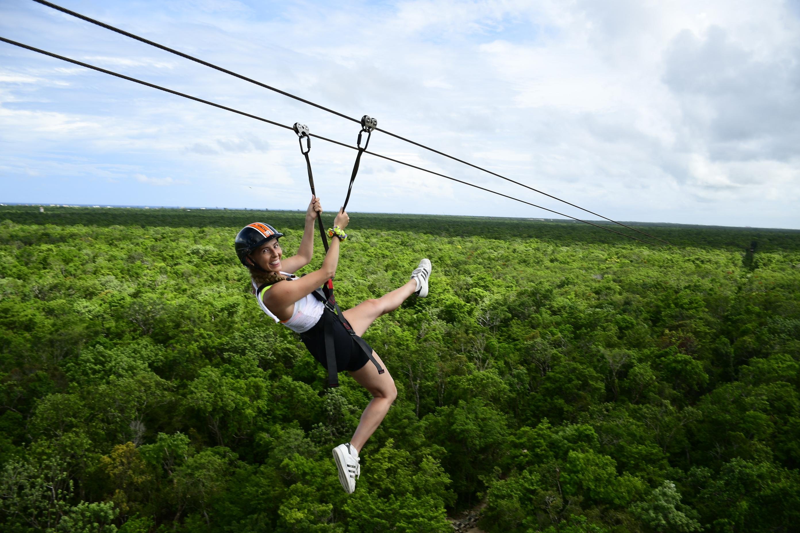 Helmeted guest riding a zipline over green jungle