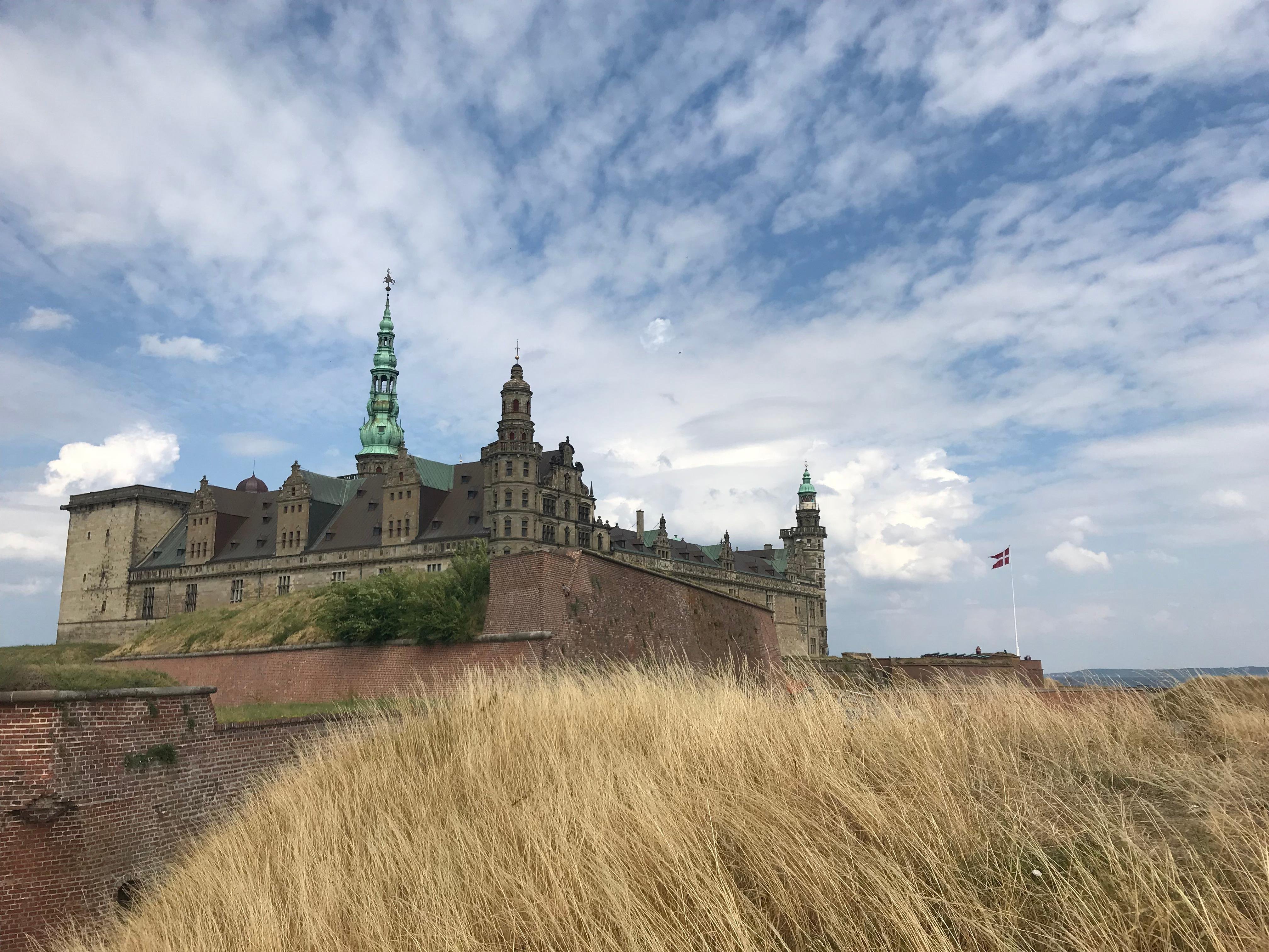 Kronborg behind its ramparts and long grass under a cloudy sky