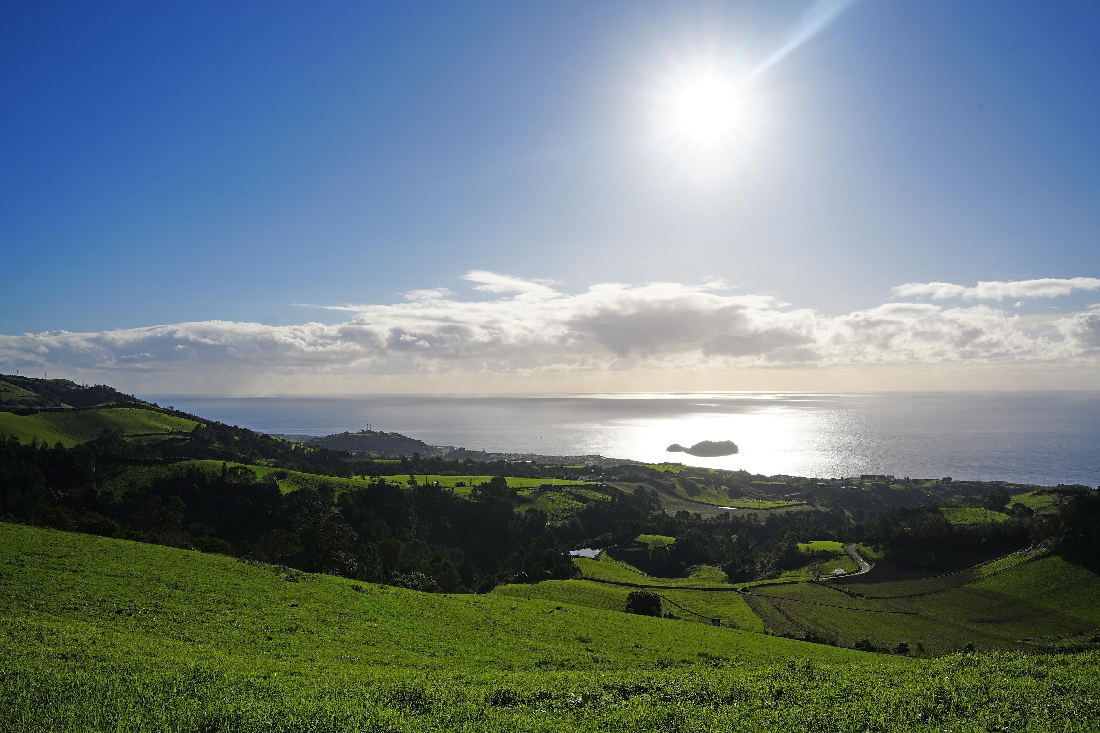 Green pasture slopes running down to the south coast of São Miguel, with an islet offshore