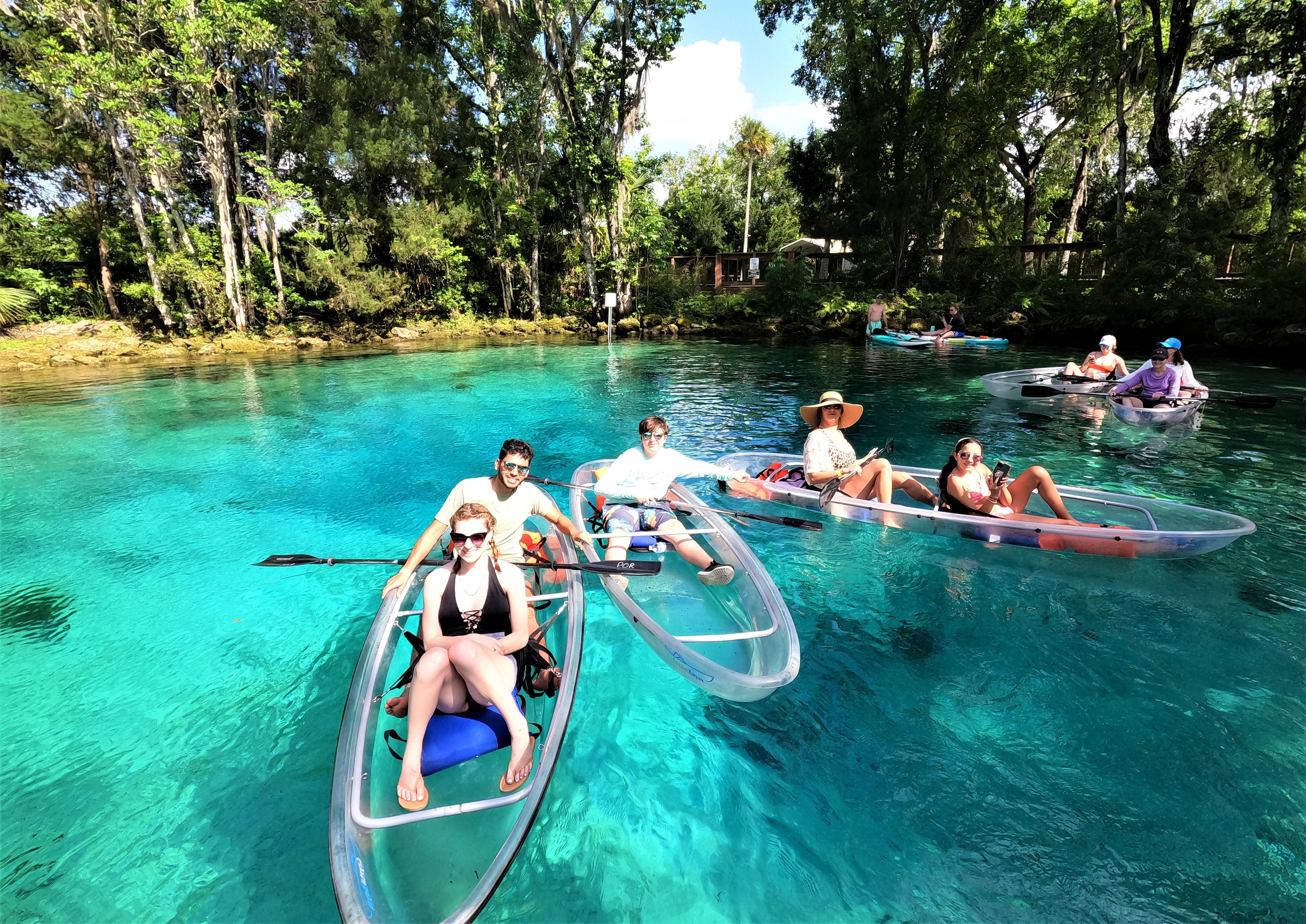Group paddling clear kayaks across sunlit spring water