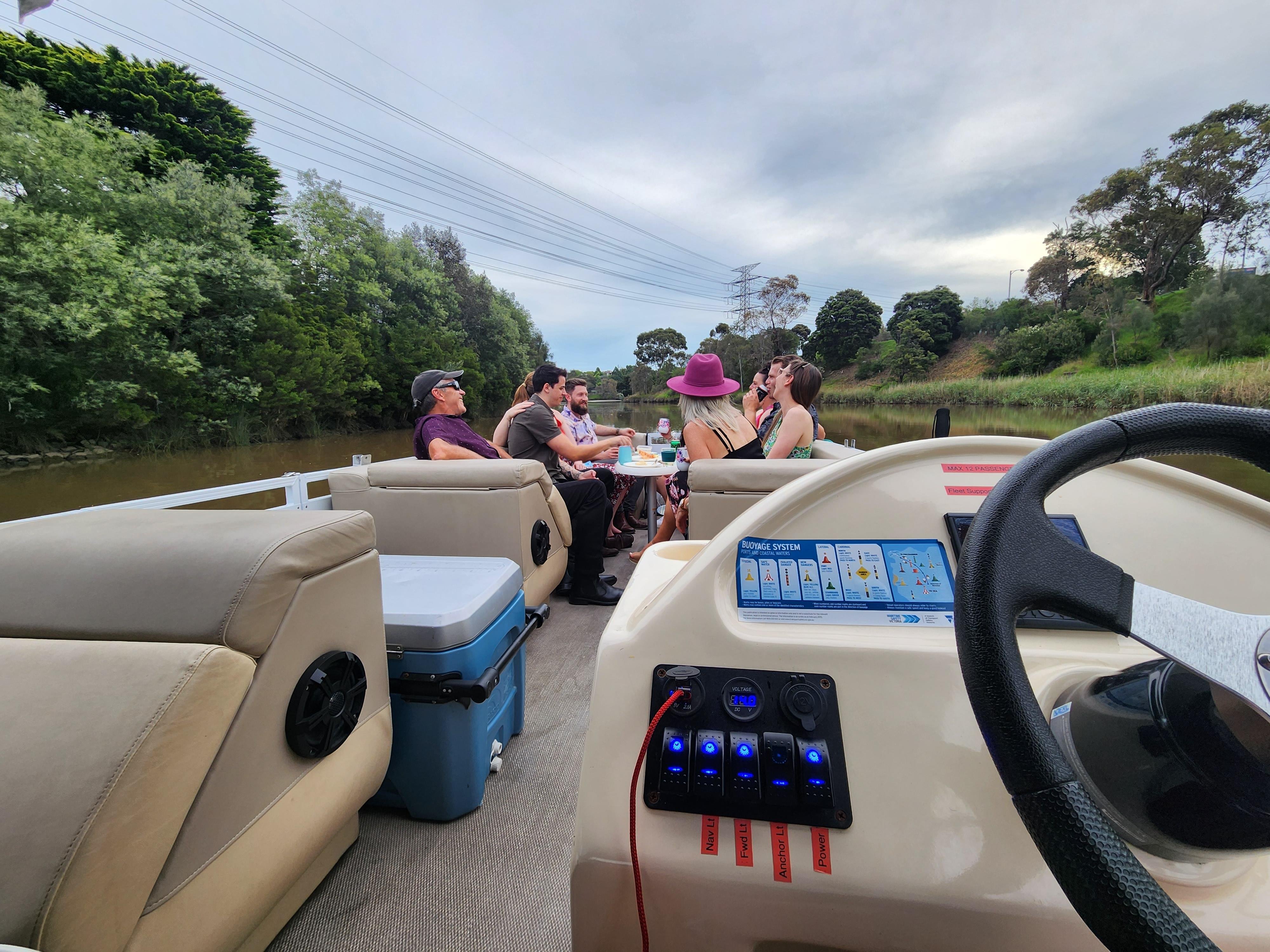 A group at the table of a BBQ pontoon boat cruising past riverside trees