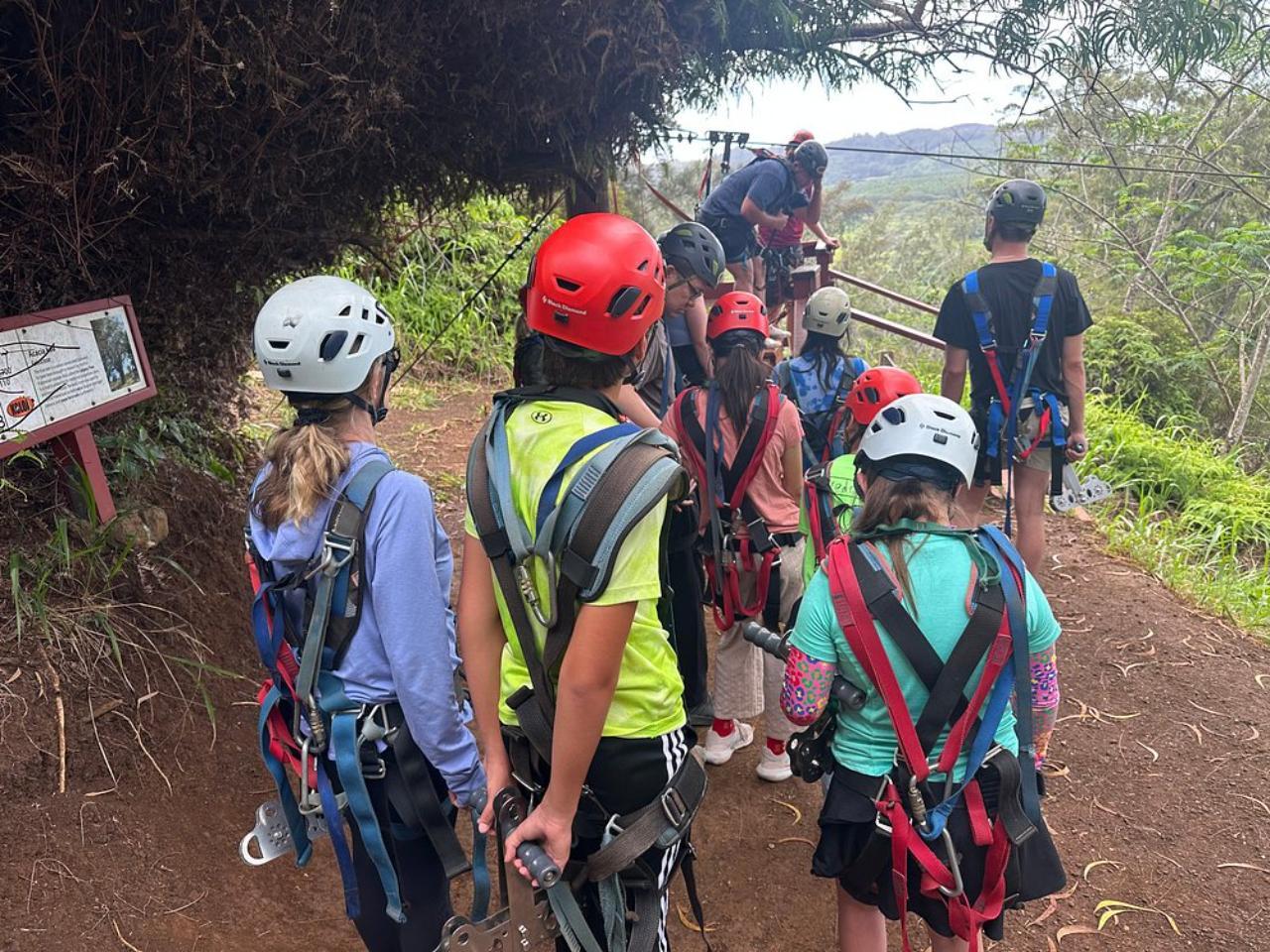 A group of helmeted guests in harnesses waiting beside a Koloa zipline platform