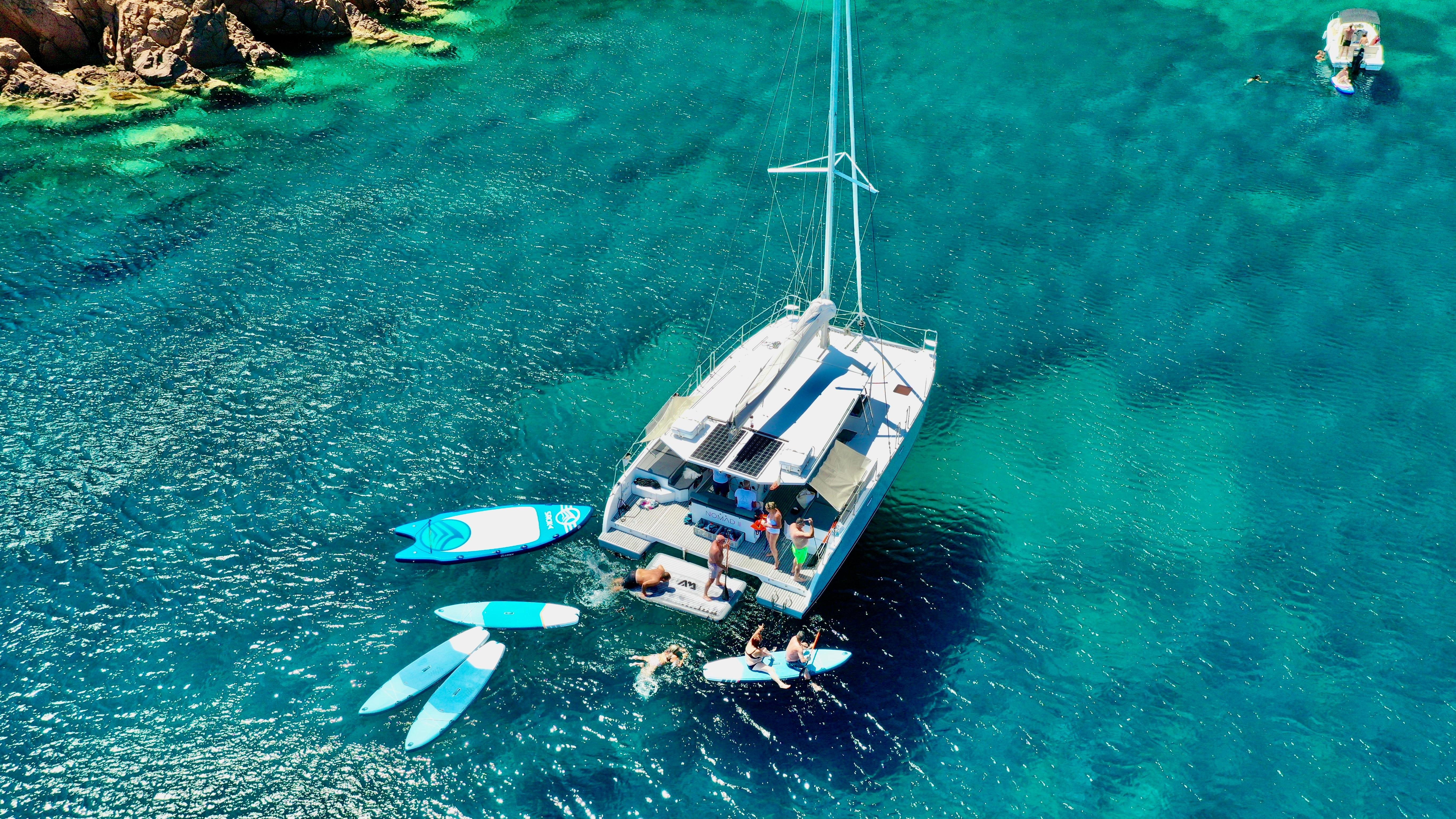 Catamaran anchored in a calanque with stand-up paddleboarders in clear blue water