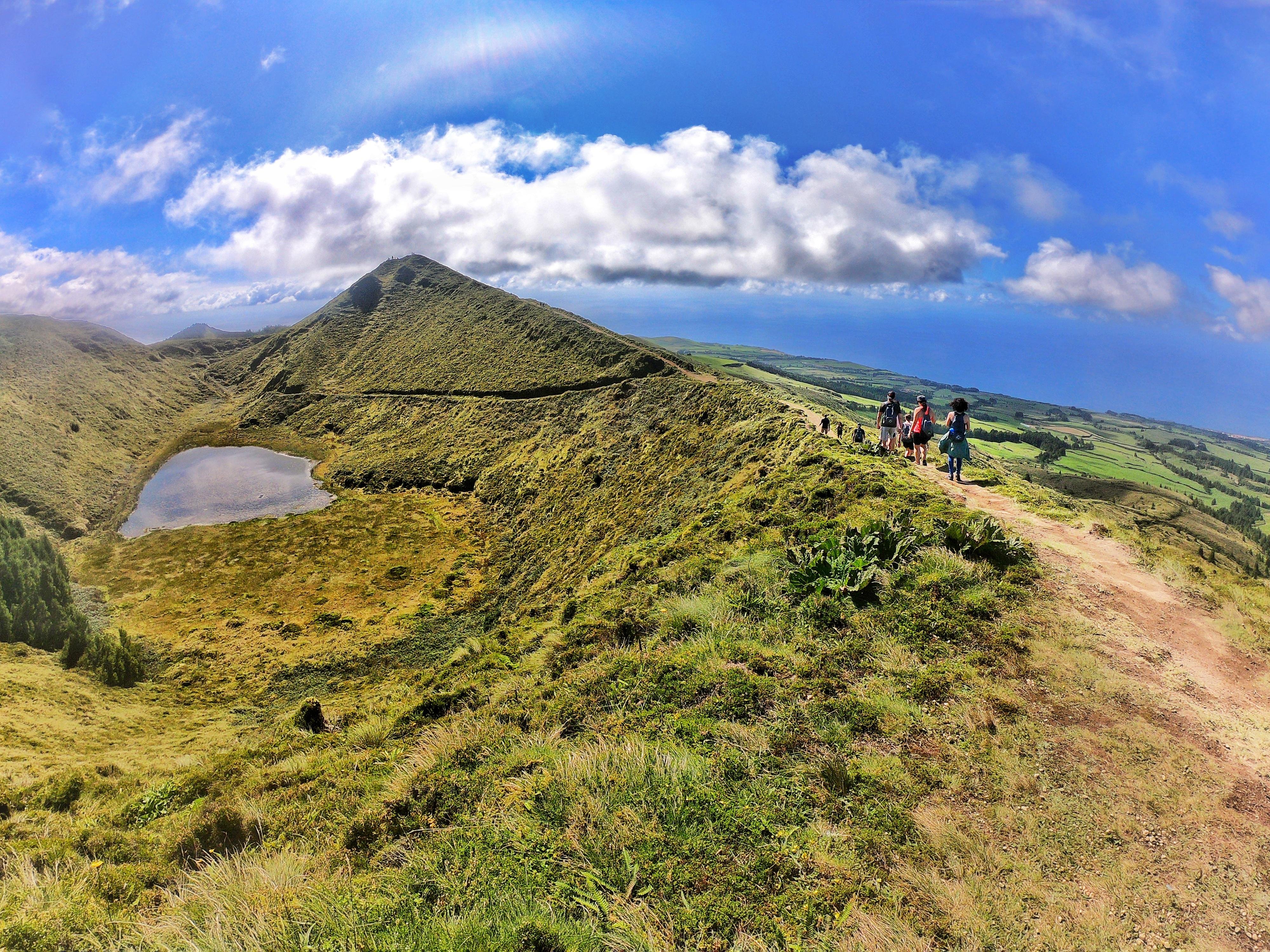 Hikers on a grassy crater ridge path above a small lake