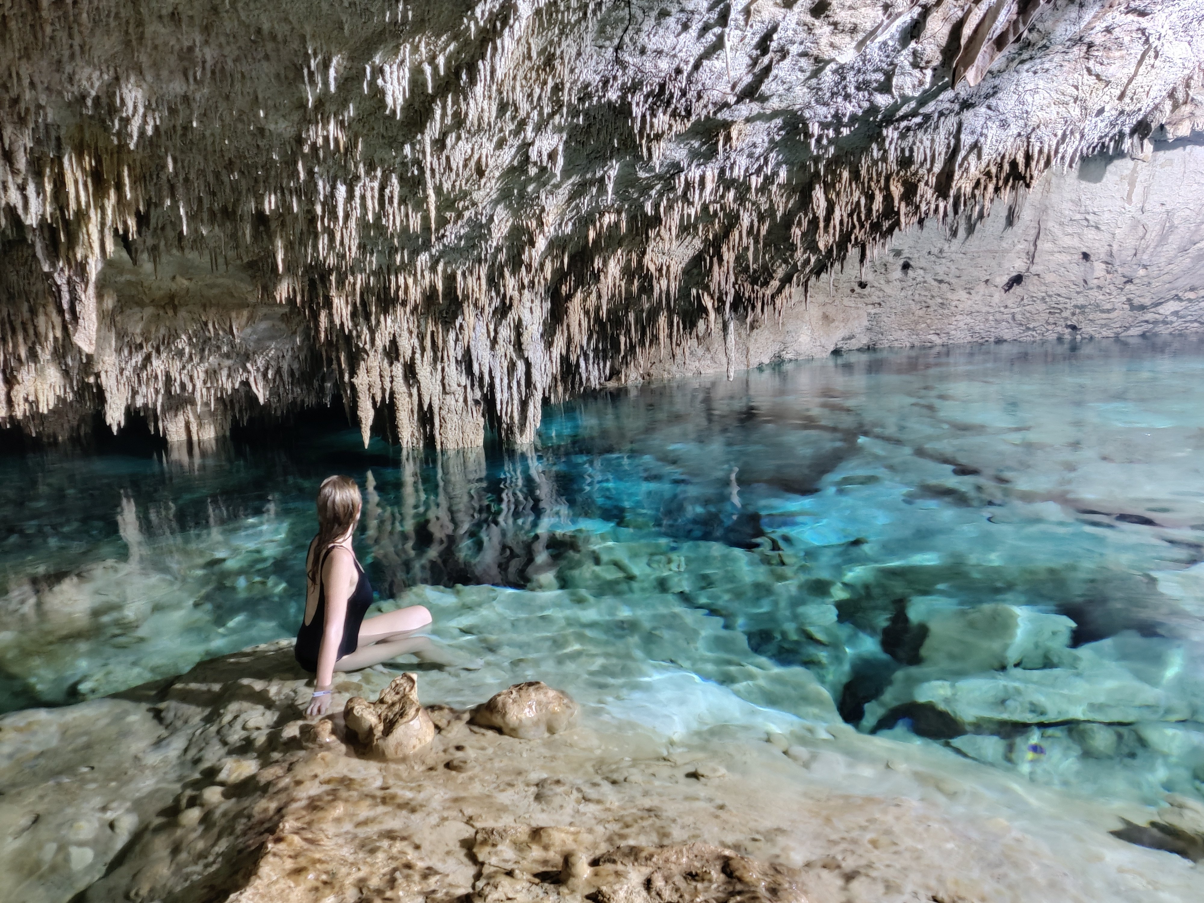 Visitor sitting beside clear water under a cave roof