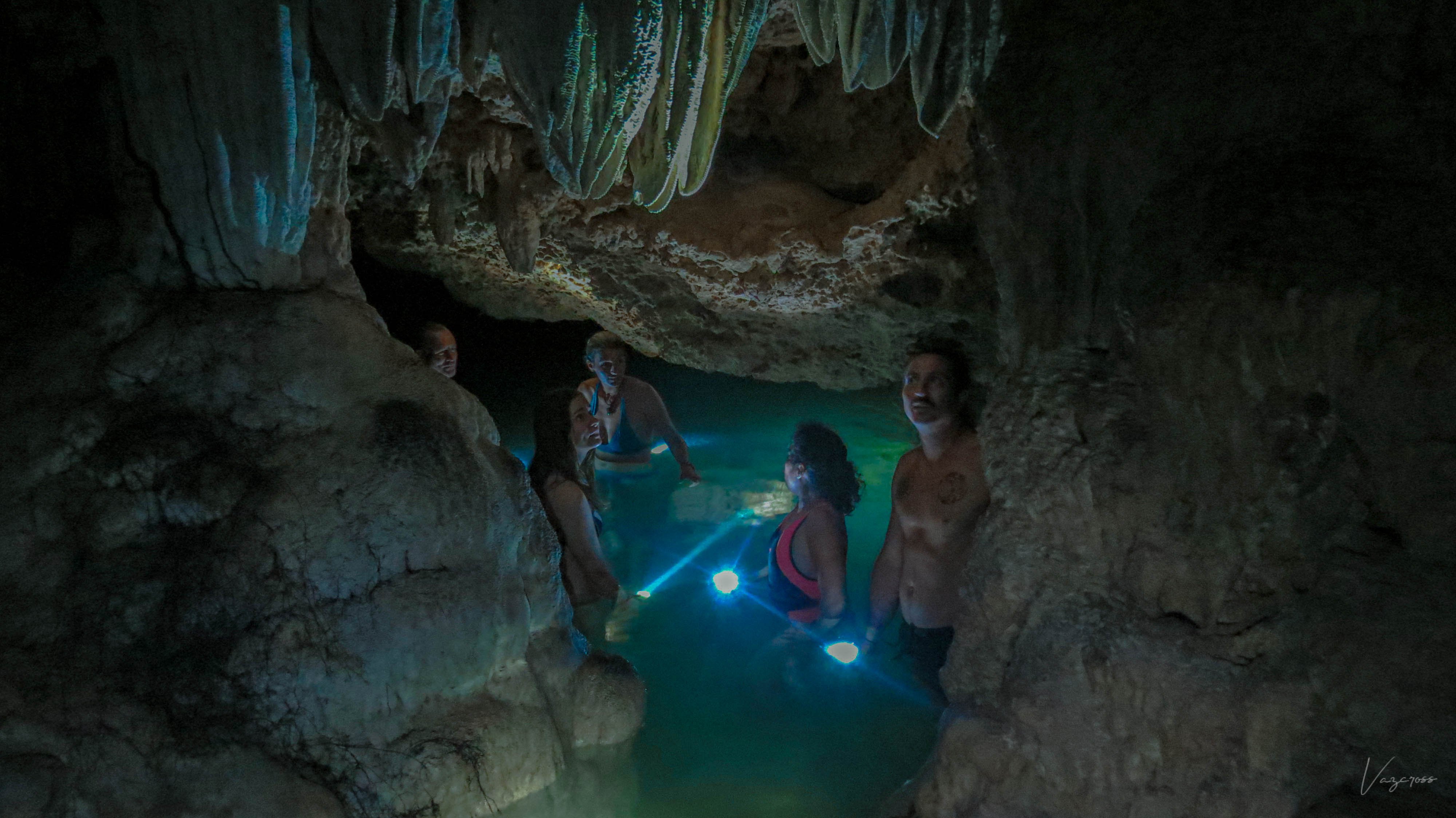 Group exploring a dark cave pool with handheld lights