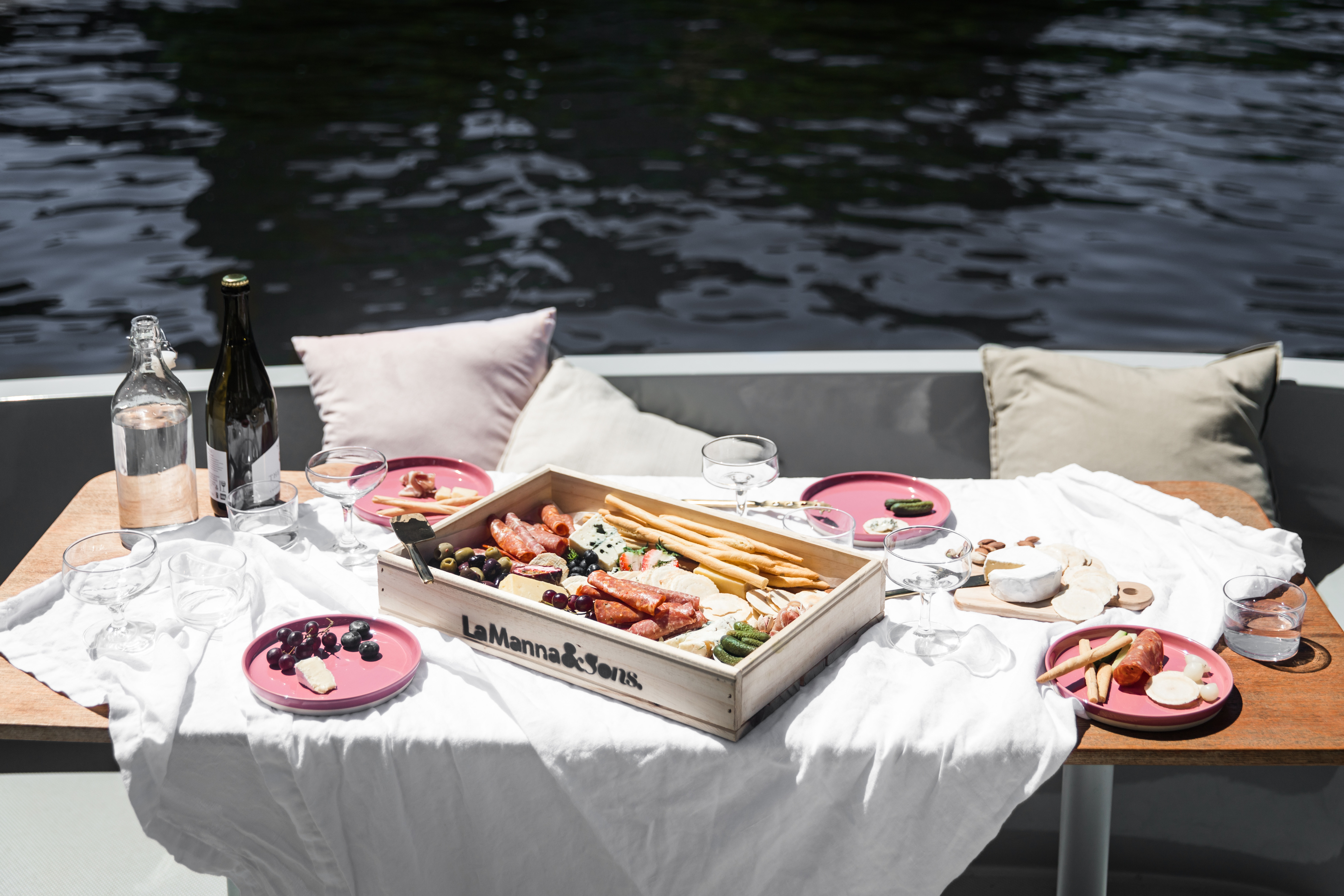 A picnic spread on a GoBoat's table: a cheese board, fruit and a bottle