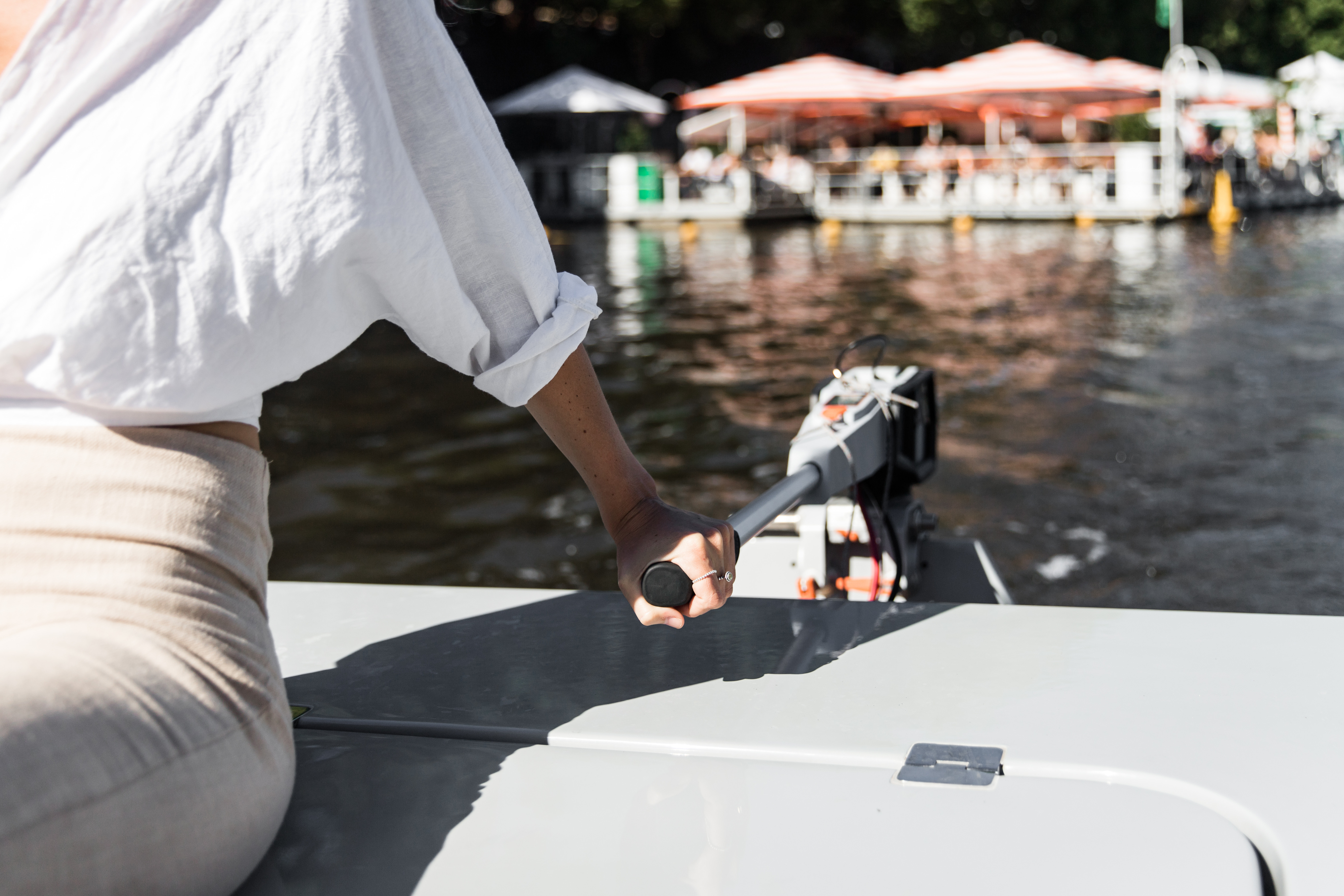 A skipper's hand on a GoBoat's tiller, a riverside bar behind