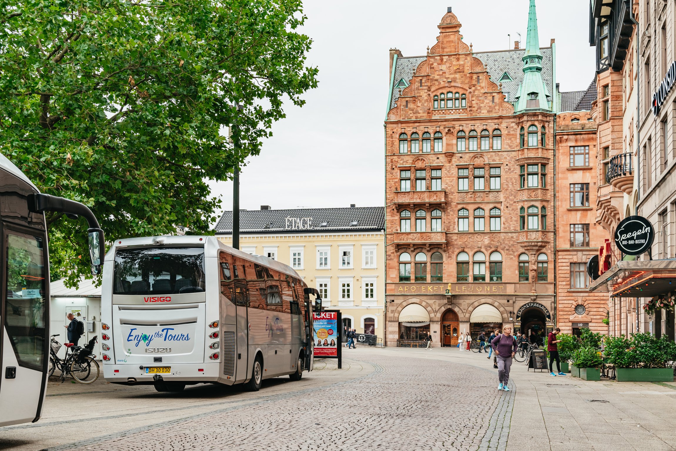 The tour coach on a cobbled street beside an ornate red sandstone building
