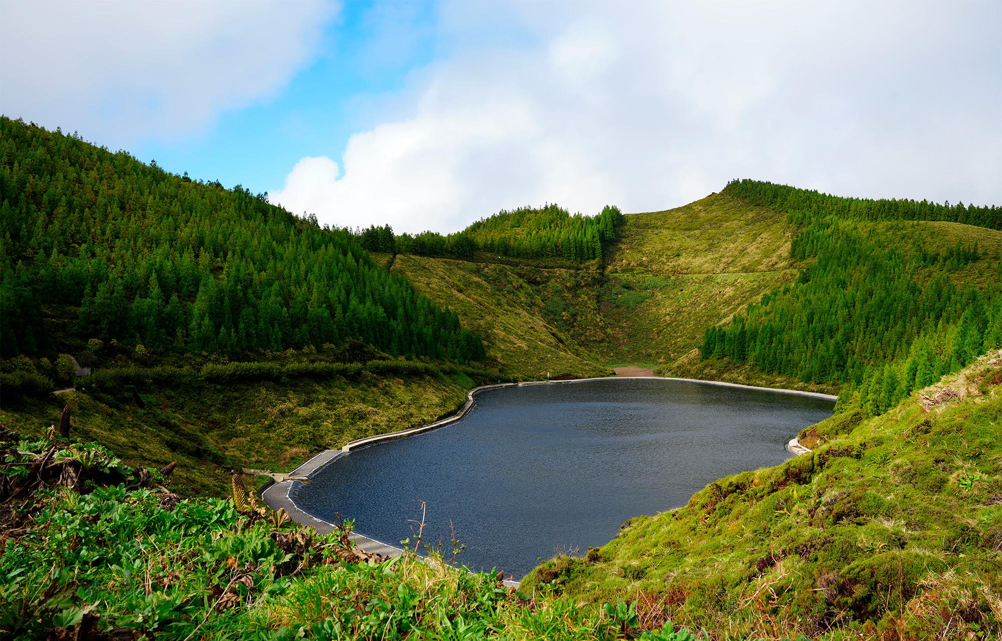 Dark volcanic lake surrounded by bright green caldera walls