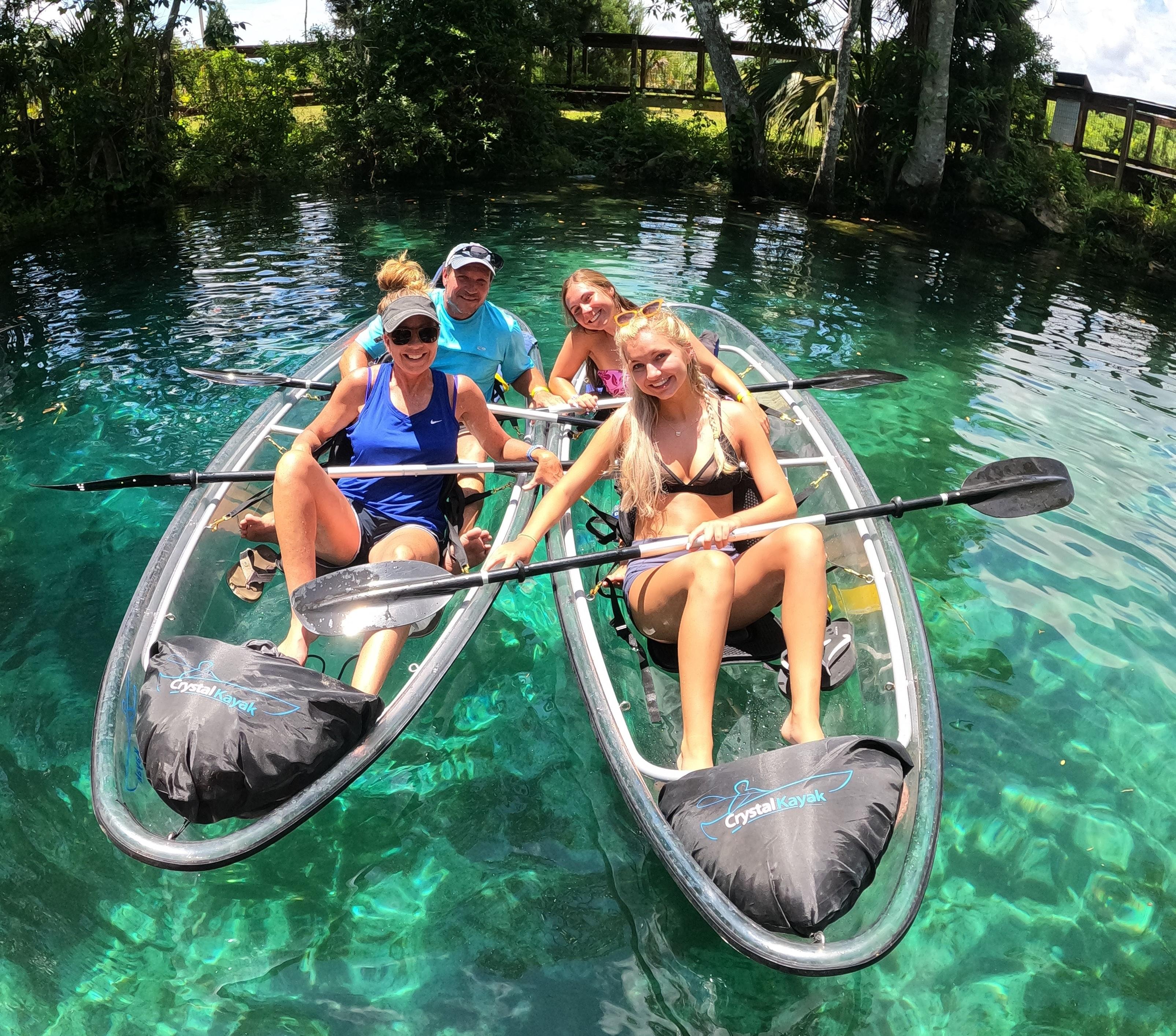 Four guests seated in two clear kayaks over transparent water