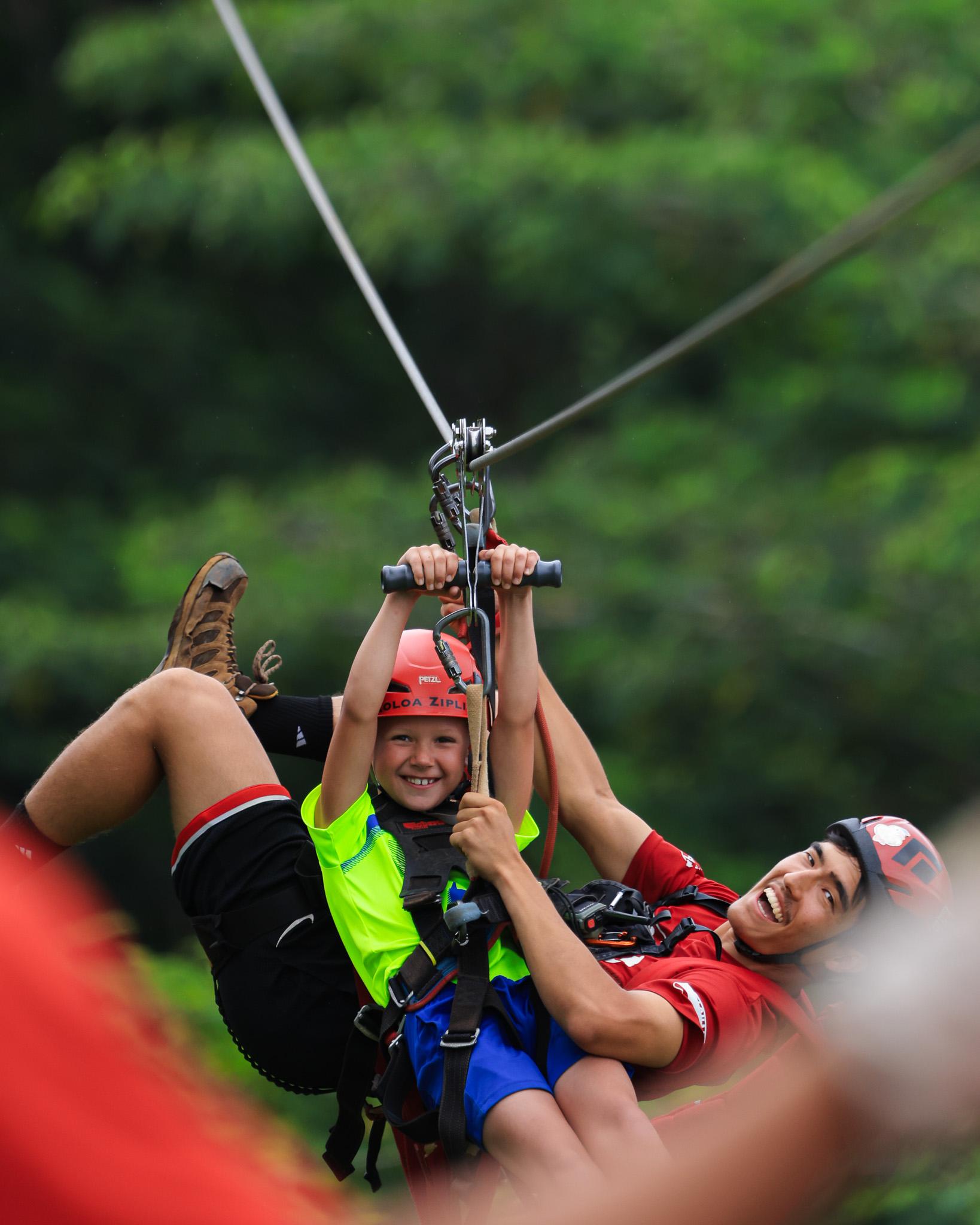 A child and an adult riding together on a Koloa zipline