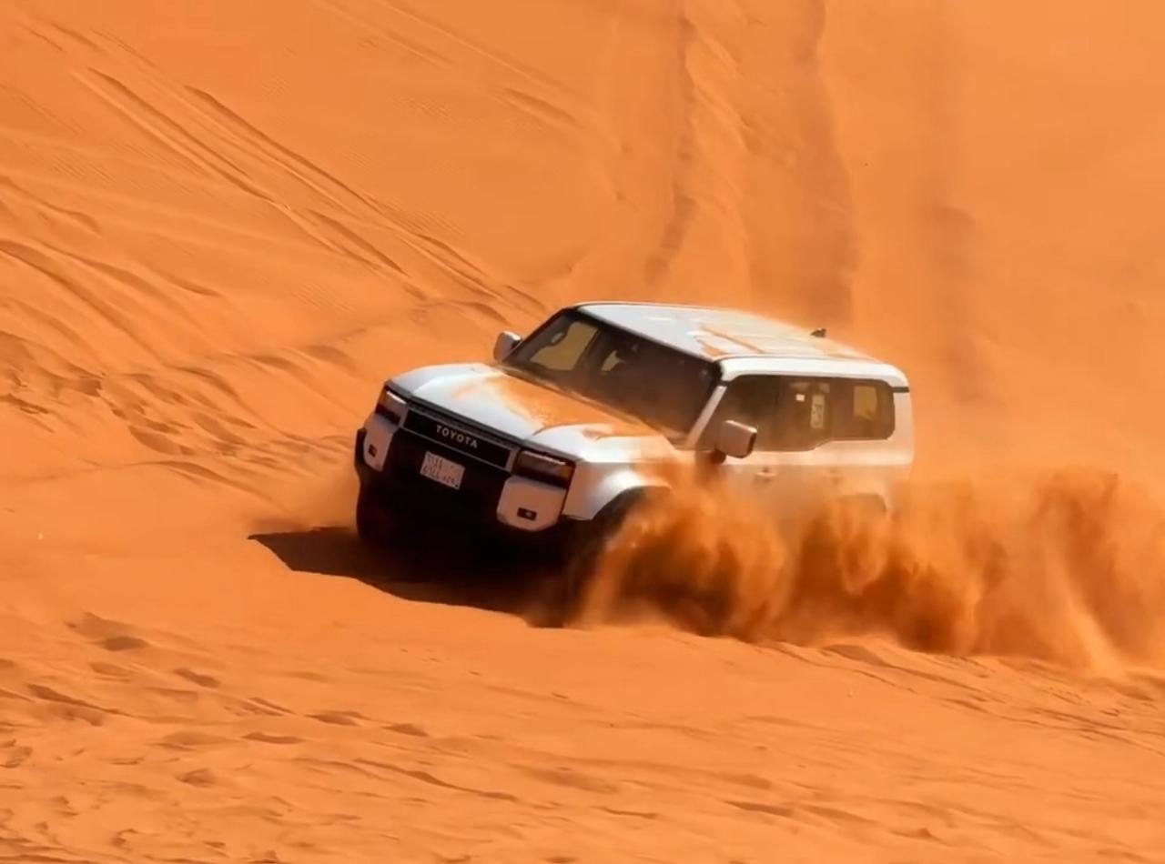 A white 4x4 charging up a steep orange dune on a Red Sand Dunes safari north of Riyadh