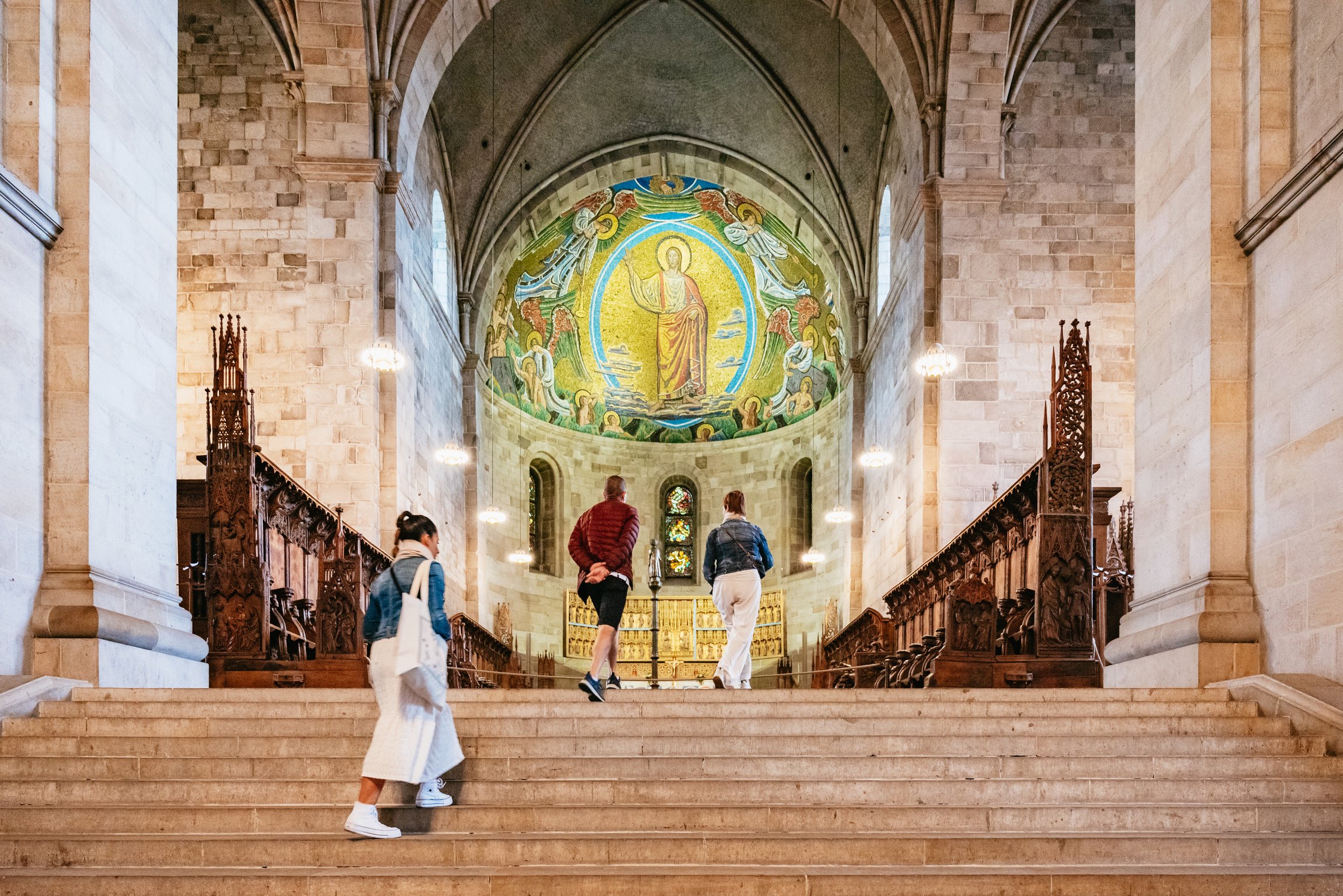 Visitors climbing the steps to the choir of Lund Cathedral under its apse mosaic
