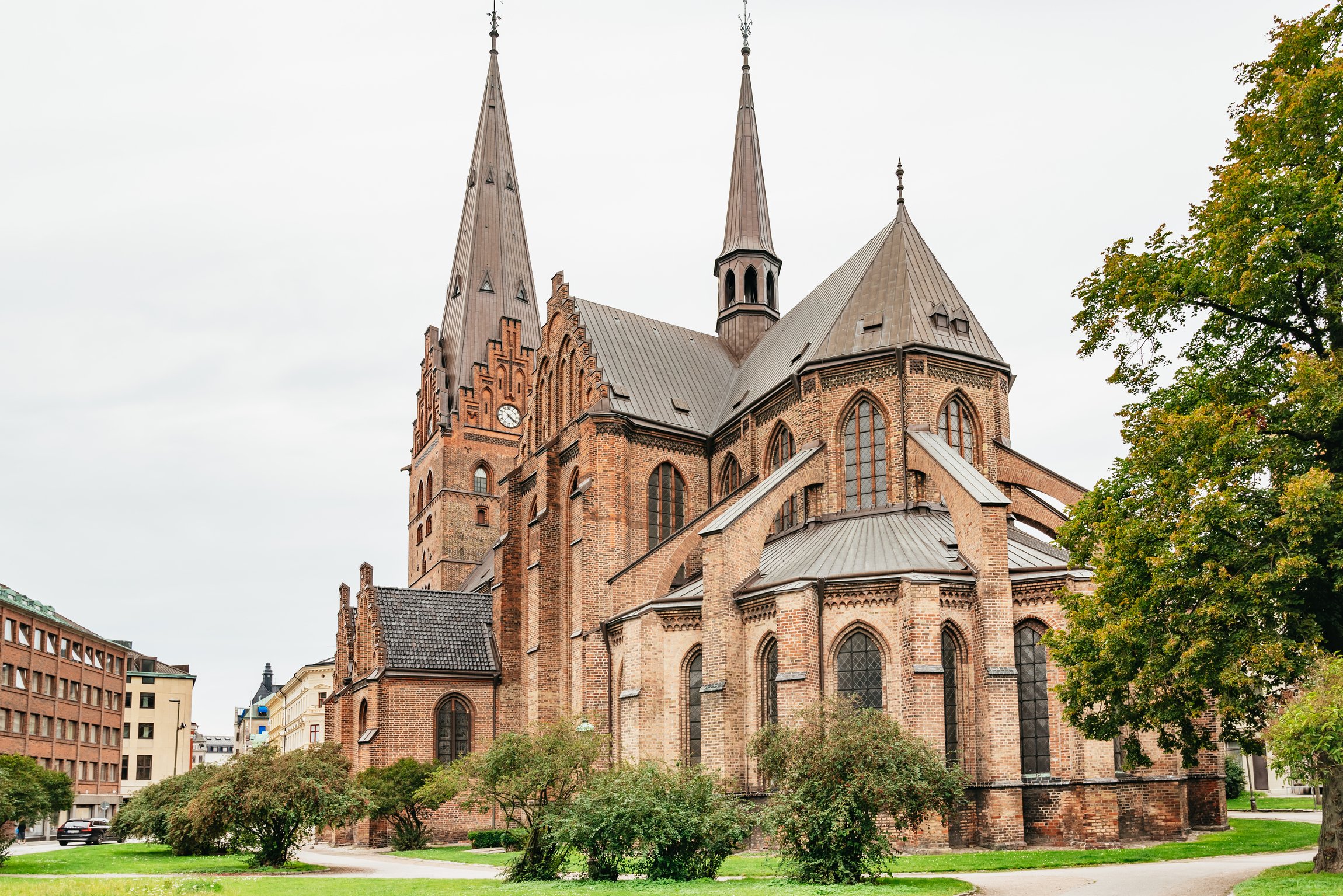 A red-brick Gothic Revival church with two spires among trees