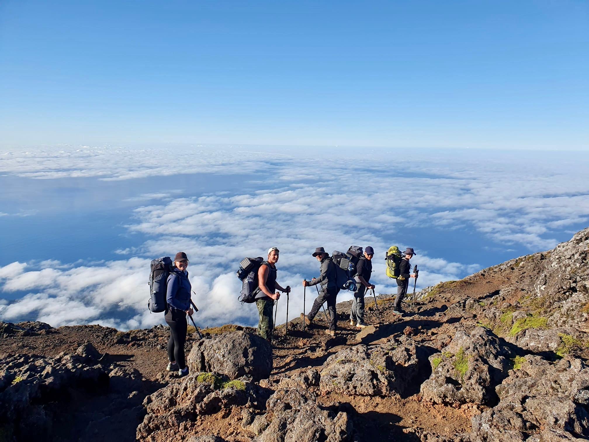Climbers with poles on a rocky slope of Pico above a sea of cloud