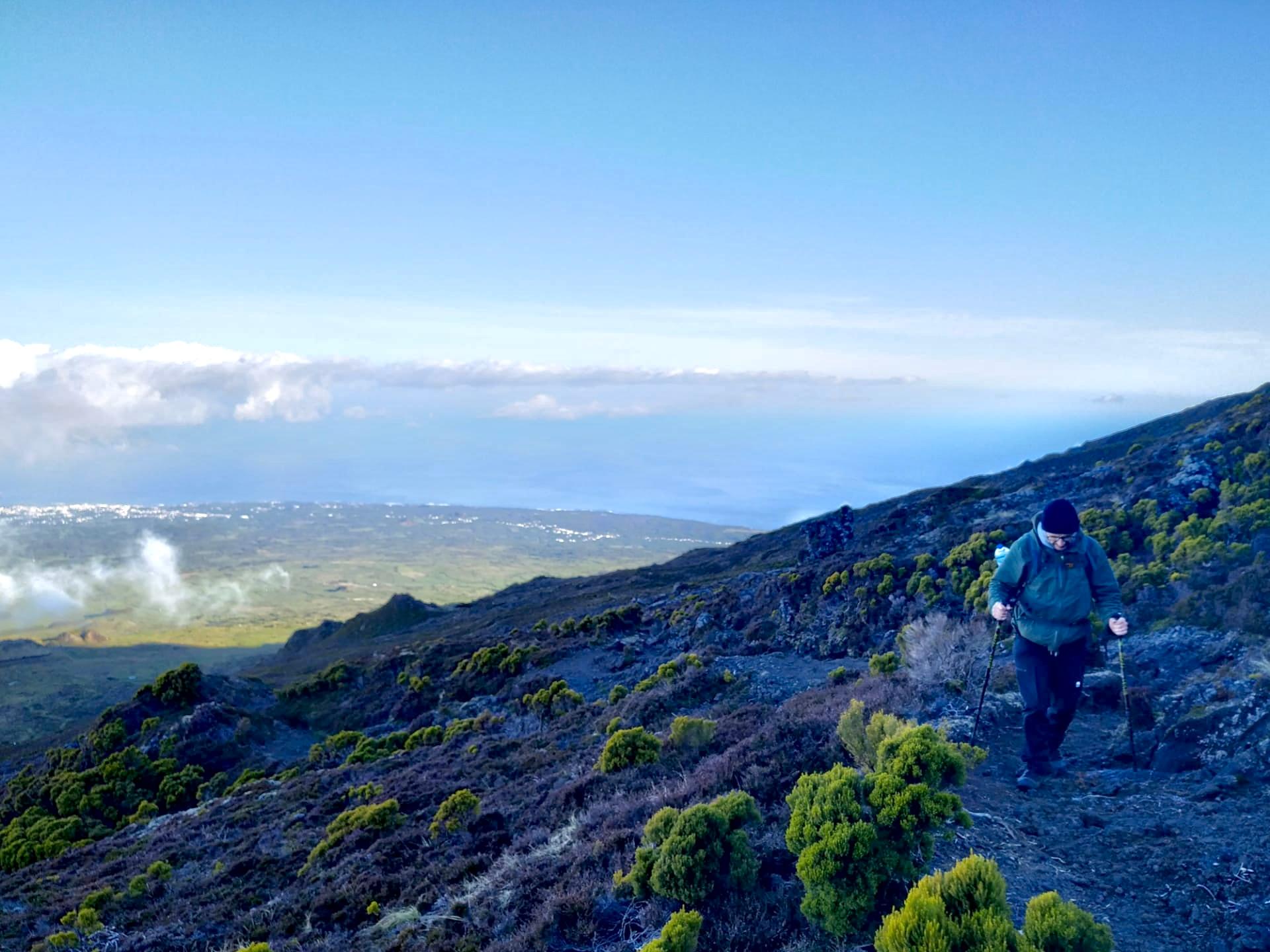 A climber descending Pico’s dark volcanic slope with the coast far below