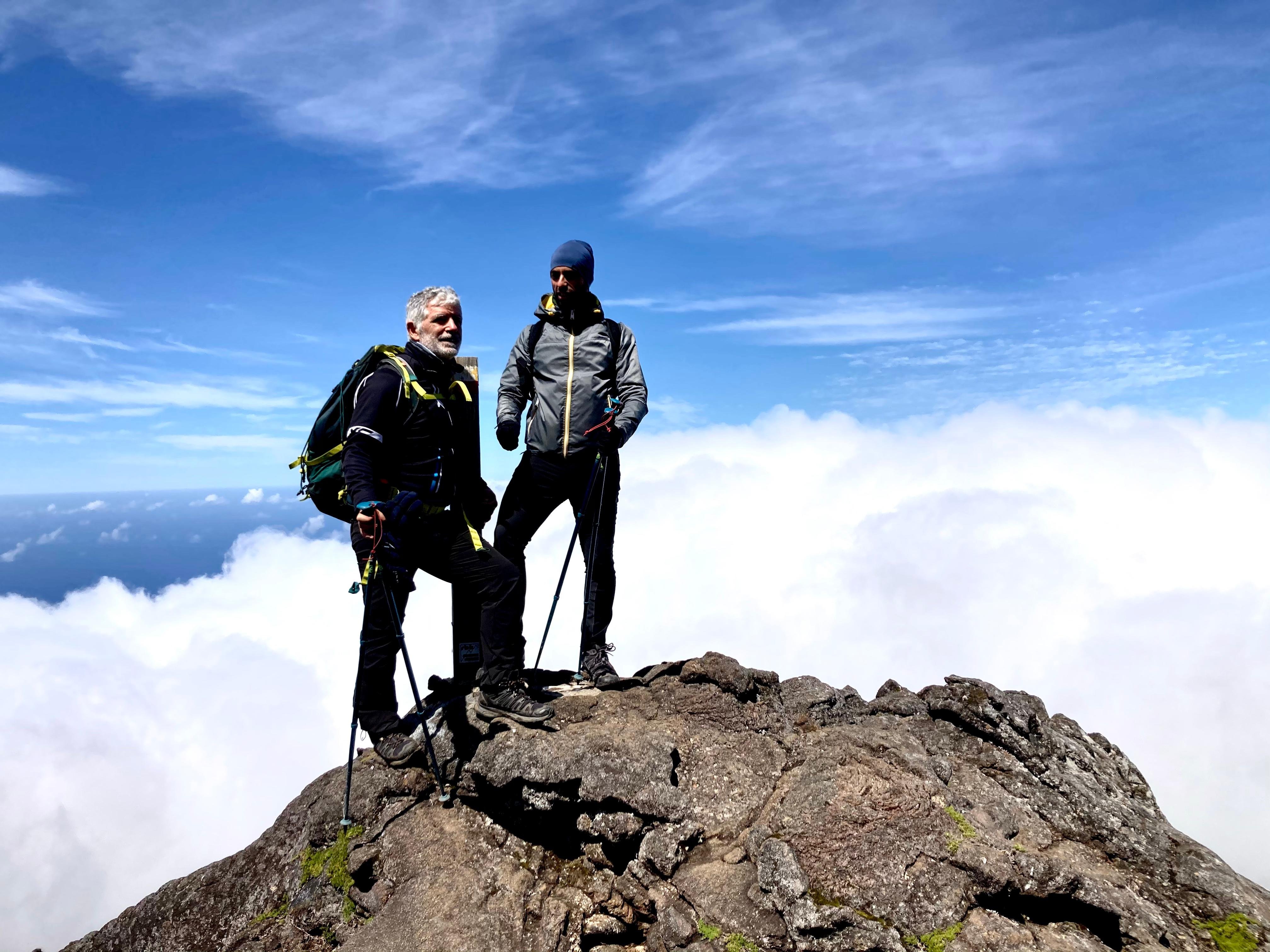 Two climbers standing on the summit rocks of Piquinho above the clouds