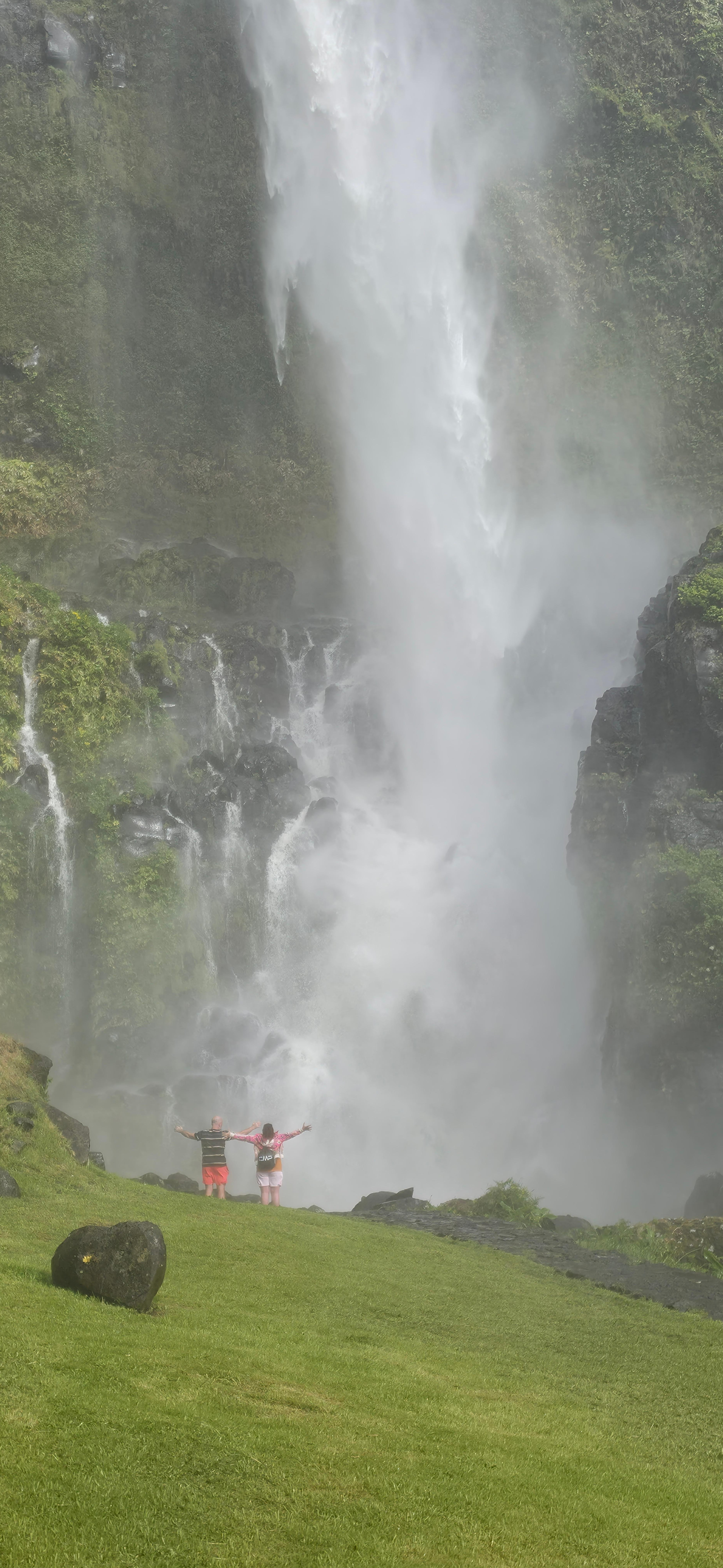 Two people at the foot of a tall waterfall on Flores