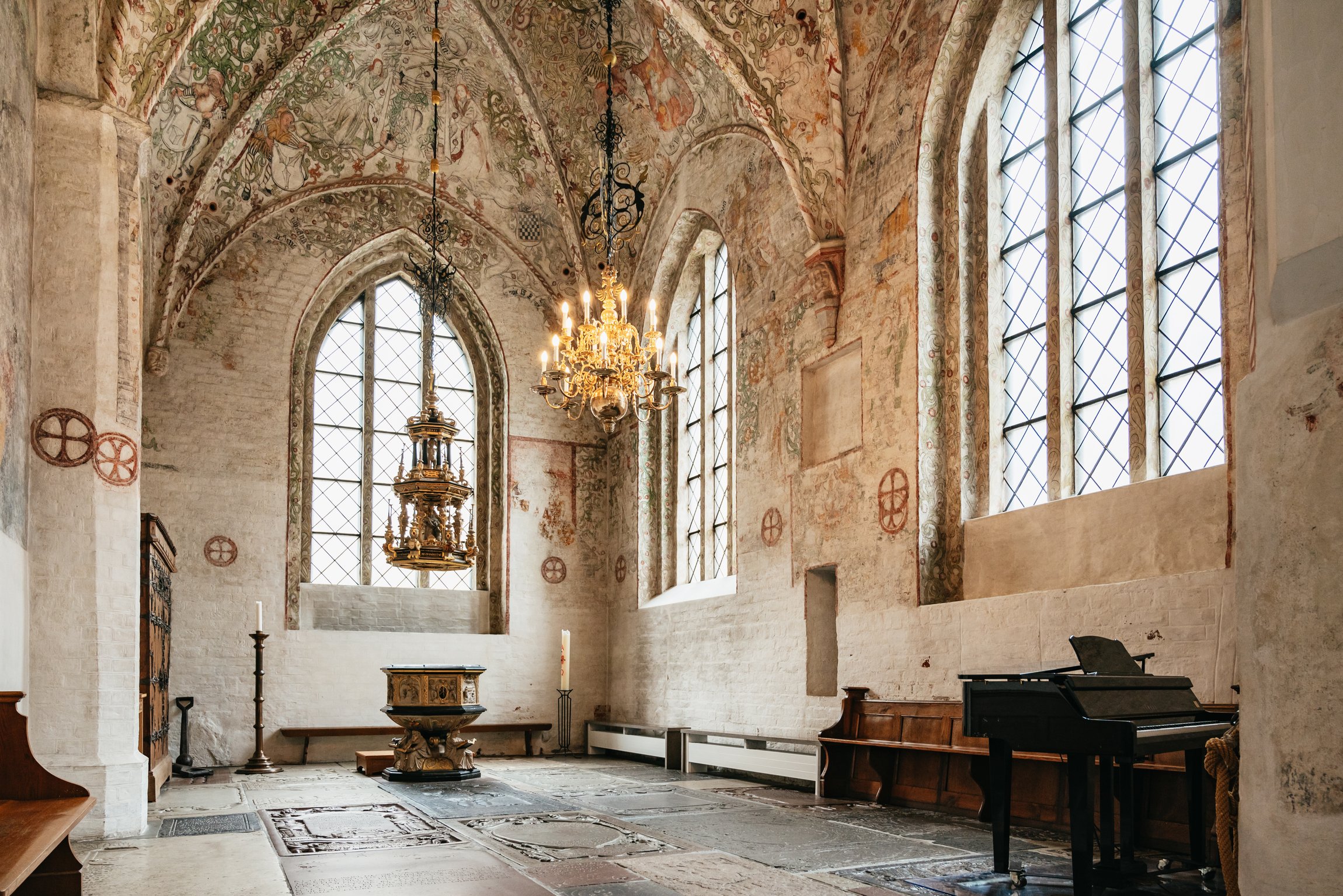 A medieval church interior with painted vaults, a chandelier and tall windows