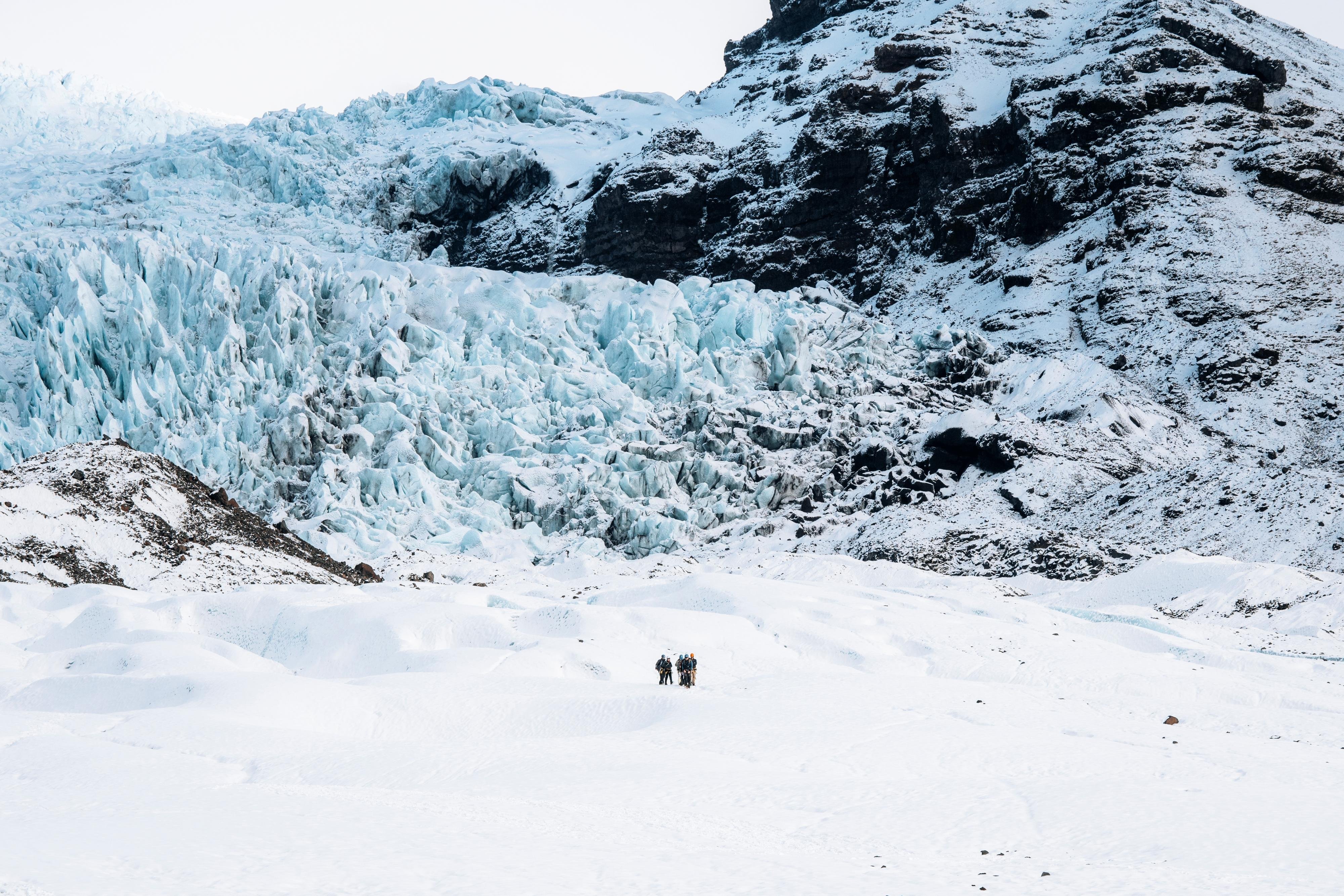 Guided hiking group crossing the snowfield toward the blue ice of Falljökull