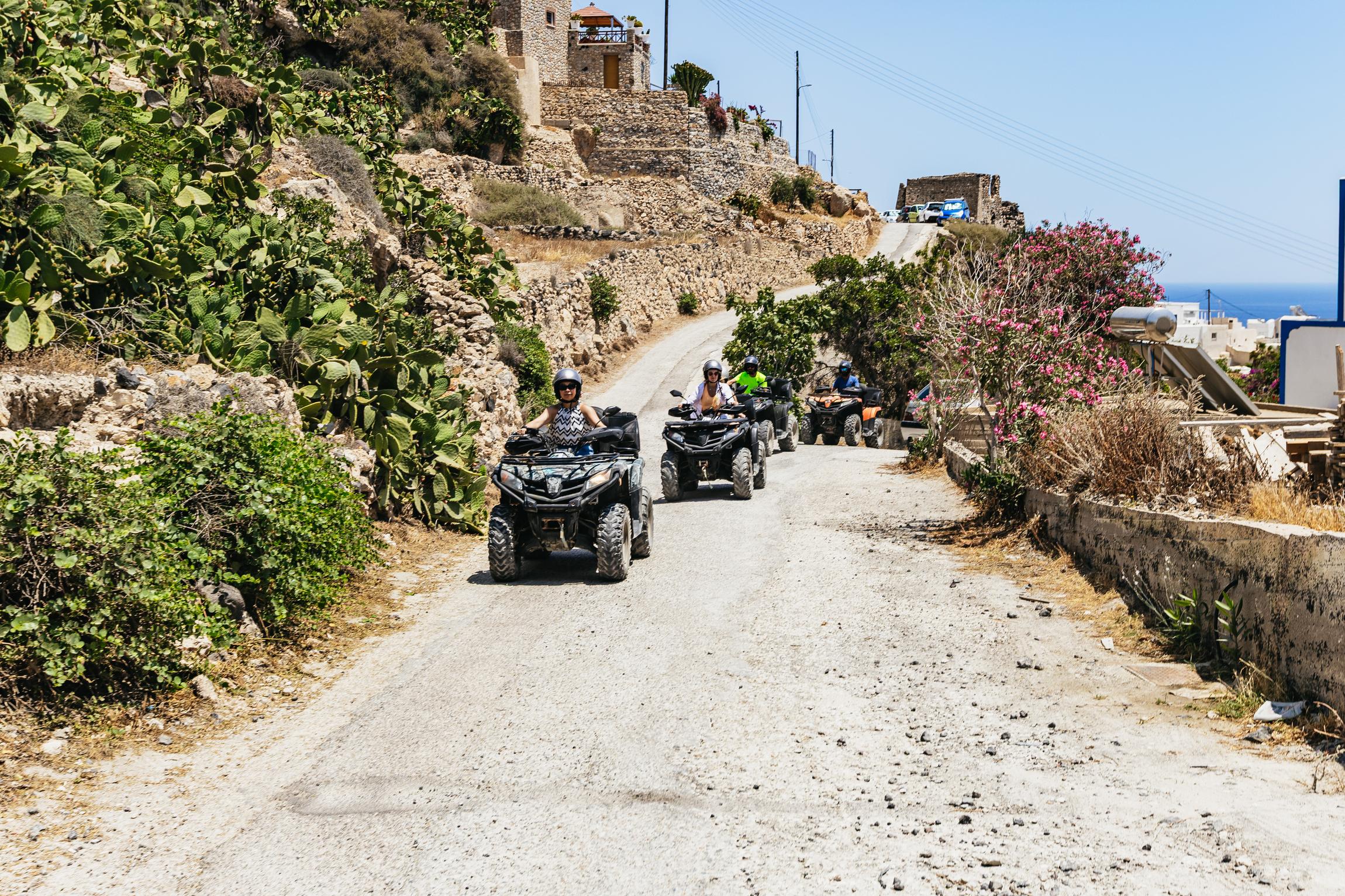 Santorini quad bike tour group on a back-road village lane with hotel pickup