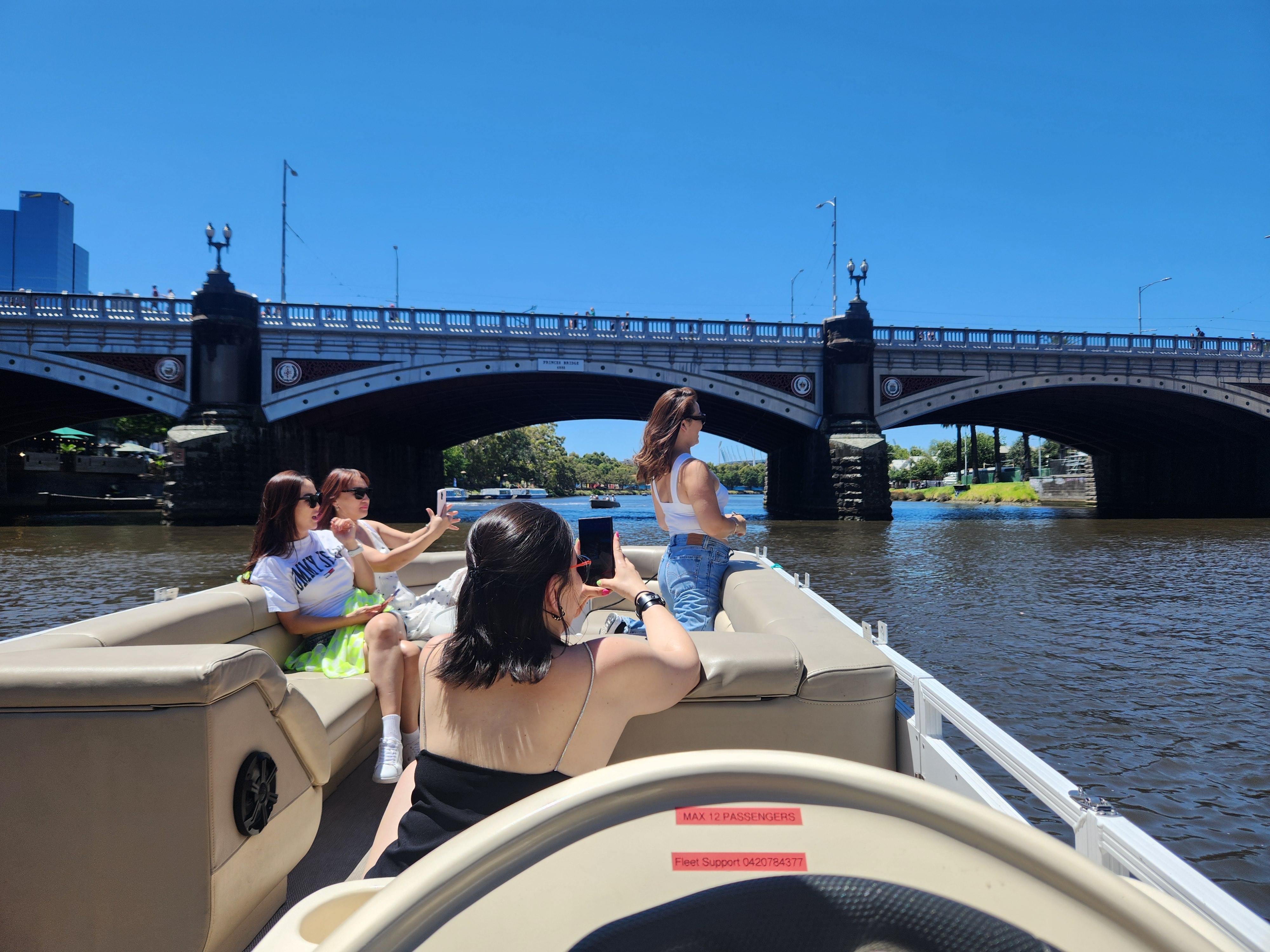 Guests at the bow of a pontoon boat taking photos near Princes Bridge