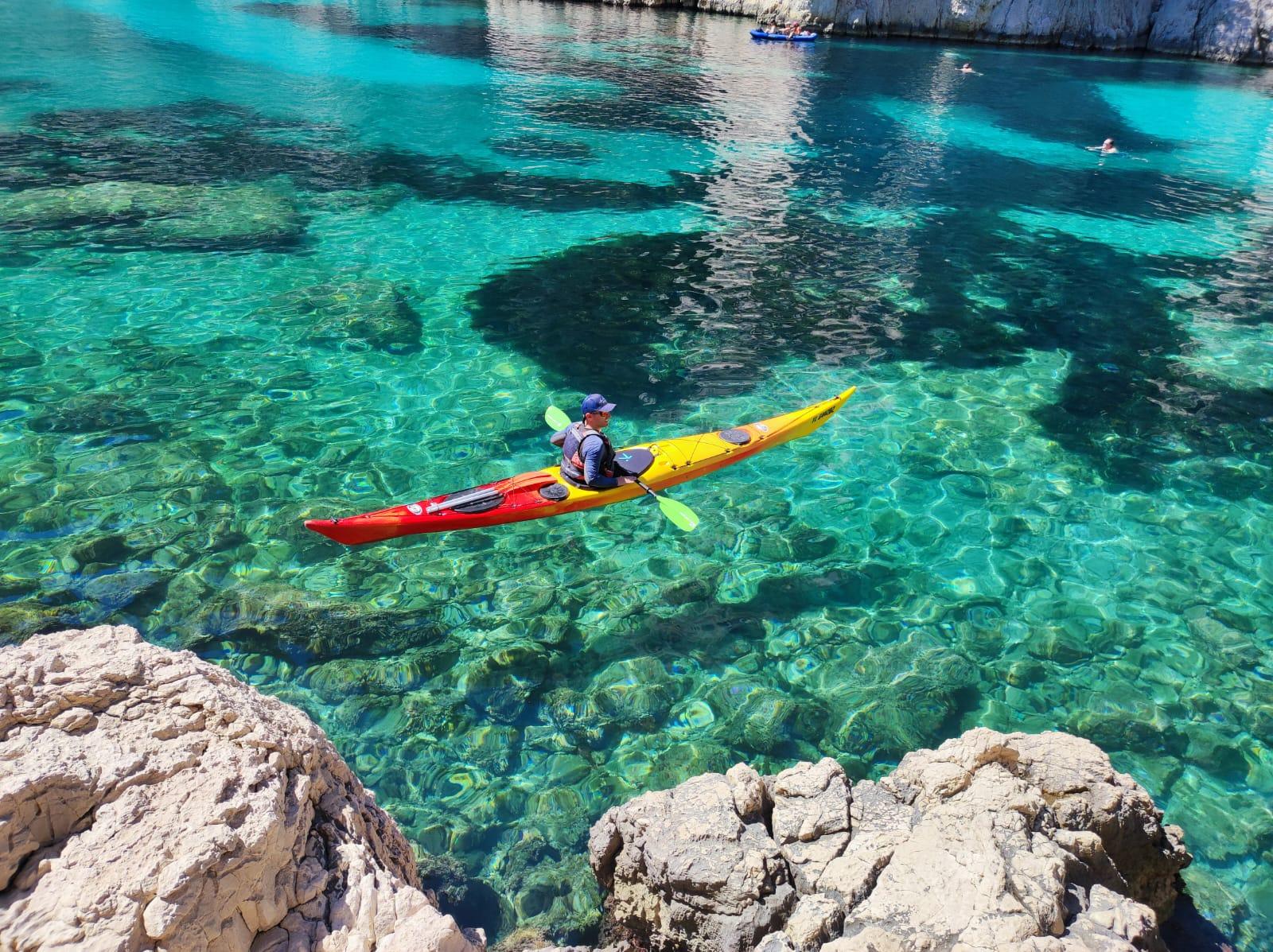 Sea kayakers paddling into a narrow calanque between high limestone walls near Cassis