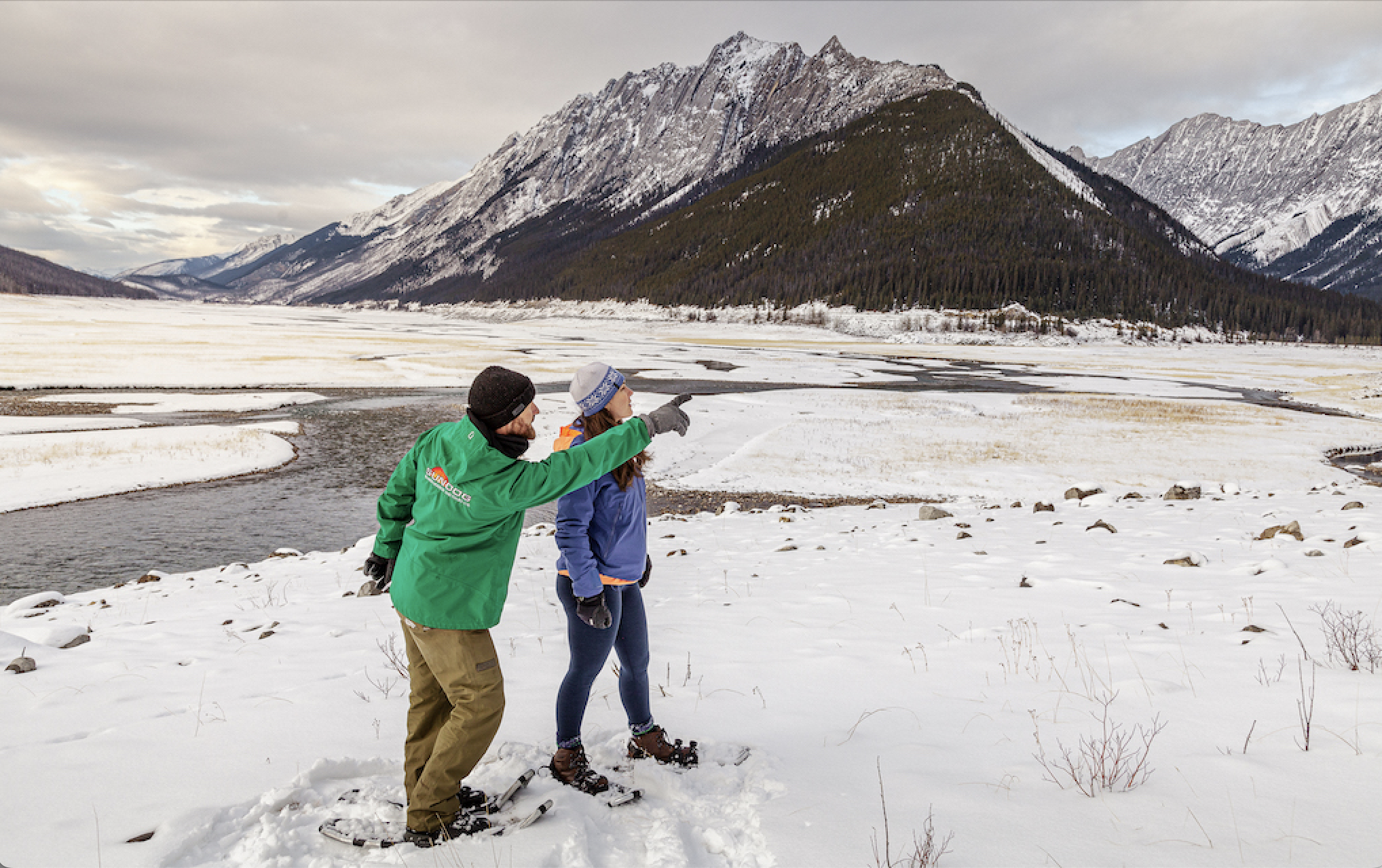 Snowshoe guide pointing out the view over a frozen, snow-covered valley floor in Jasper National Park
