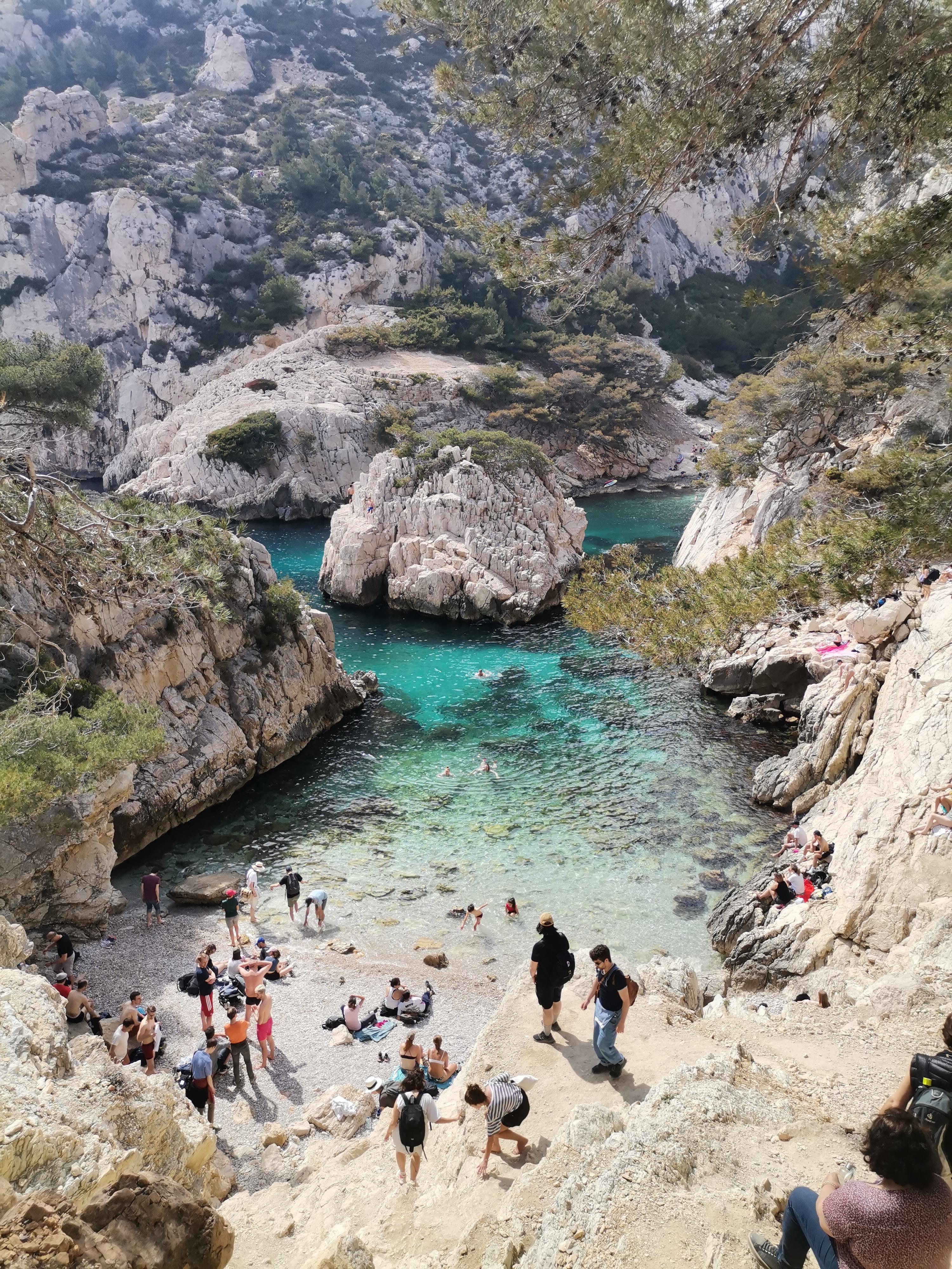 Hikers on a limestone trail above a turquoise calanque in the Calanques National Park