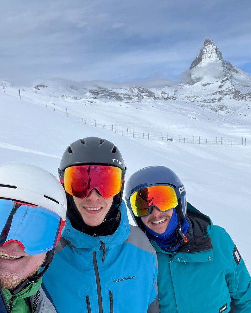 Tre skiløbere med hjelme og skibriller tæt sammen, og Matterhorn rejser sig bagved