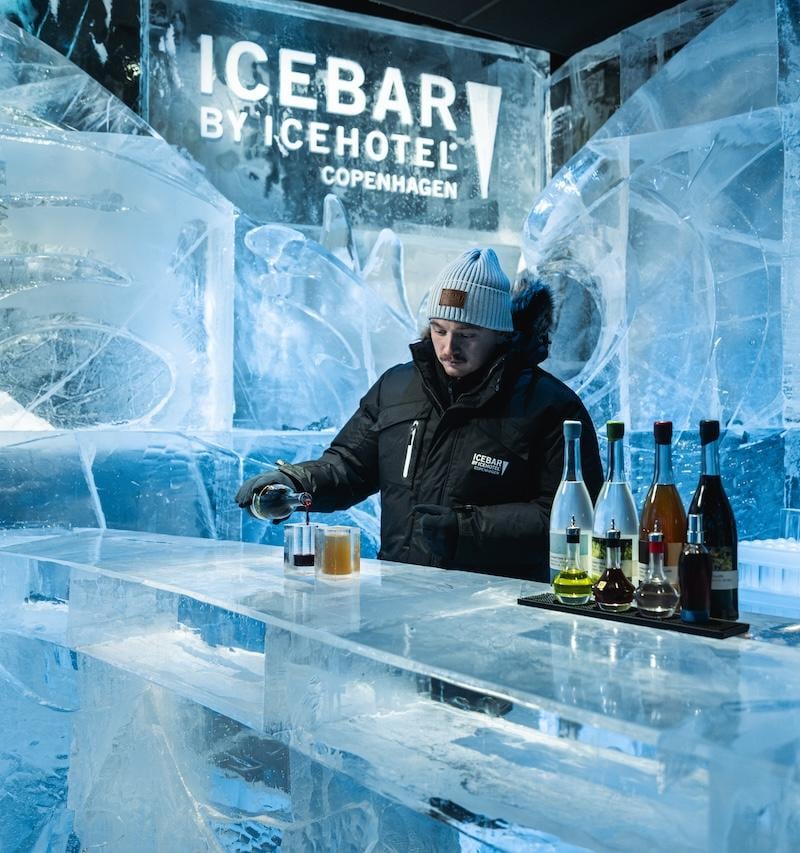 Bartender bag en bardisk af is med flasker og ICEBAR-logoet på væggen af is