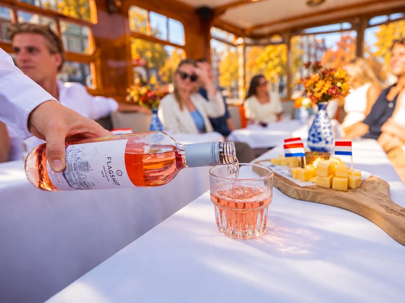 Rosévin hældes i et glas ved siden af en tallerken med ost på en salonbåd