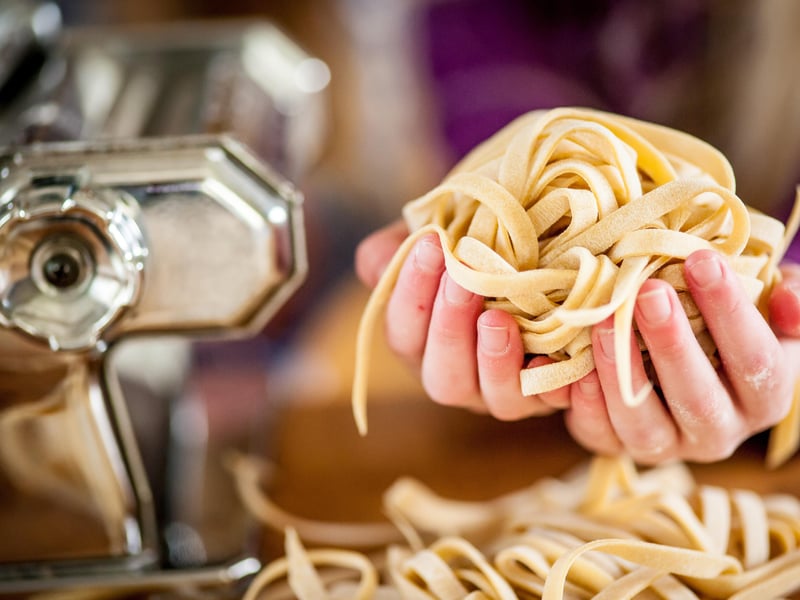 Hånd holder friskrullet pasta ved siden af en pastamaskine