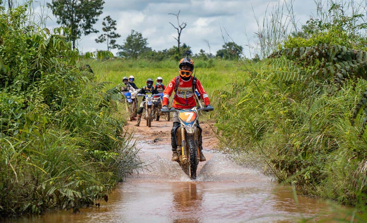 Dirt-bike riders crossing a muddy trail in the Cambodian countryside near Siem Reap