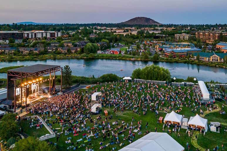 A large outdoor concert in a field near a river.