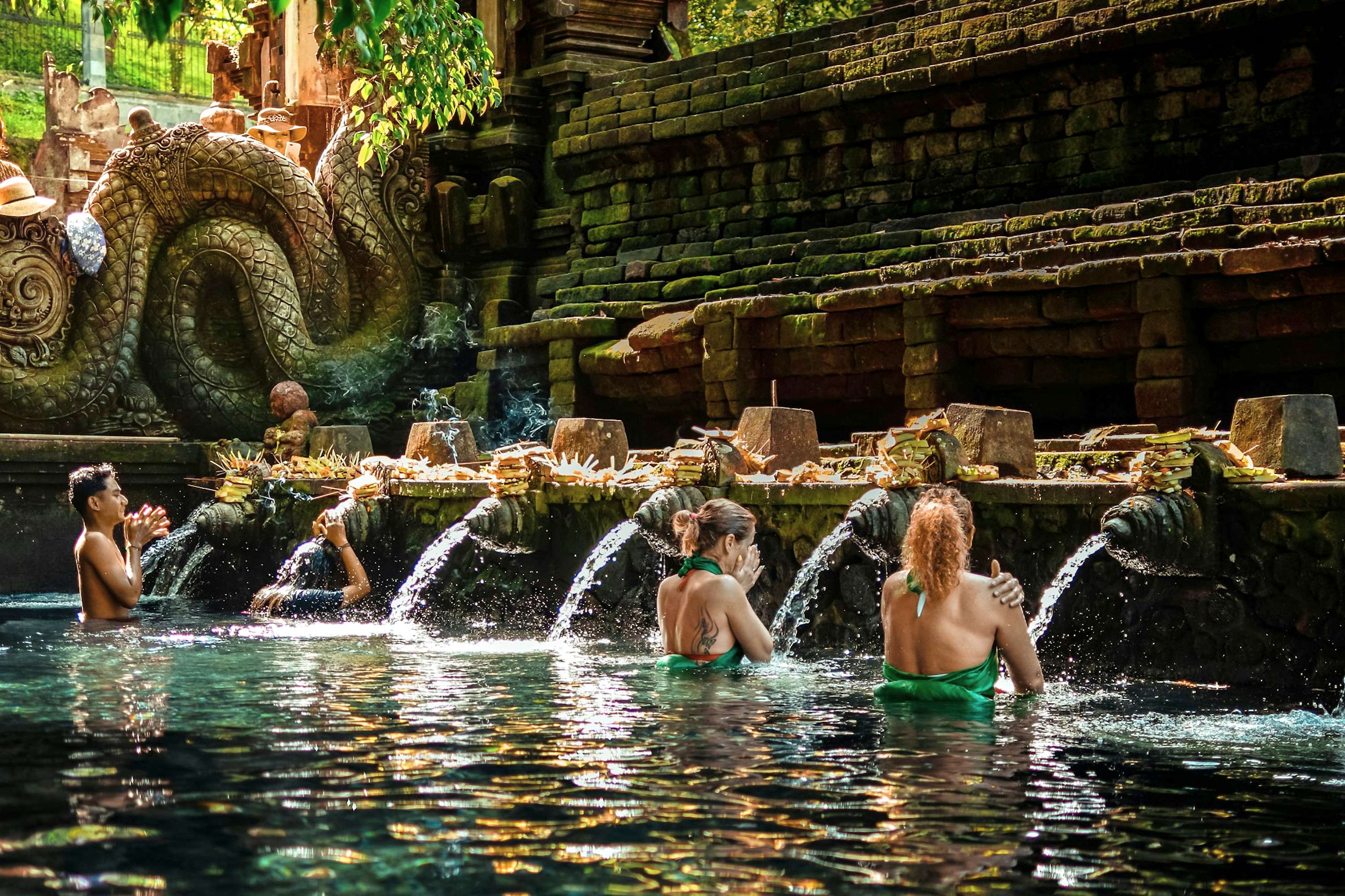 People bathing at Tirta Empul Temple purification pools under stone water spouts.