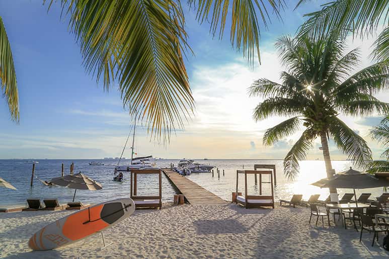 Una playa en Isla Mujeres con palmeras y barcos.