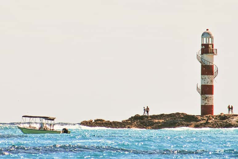 Vista del faro rojo y blanco de Punta Cancún rodeado de resplandecientes aguas azules.