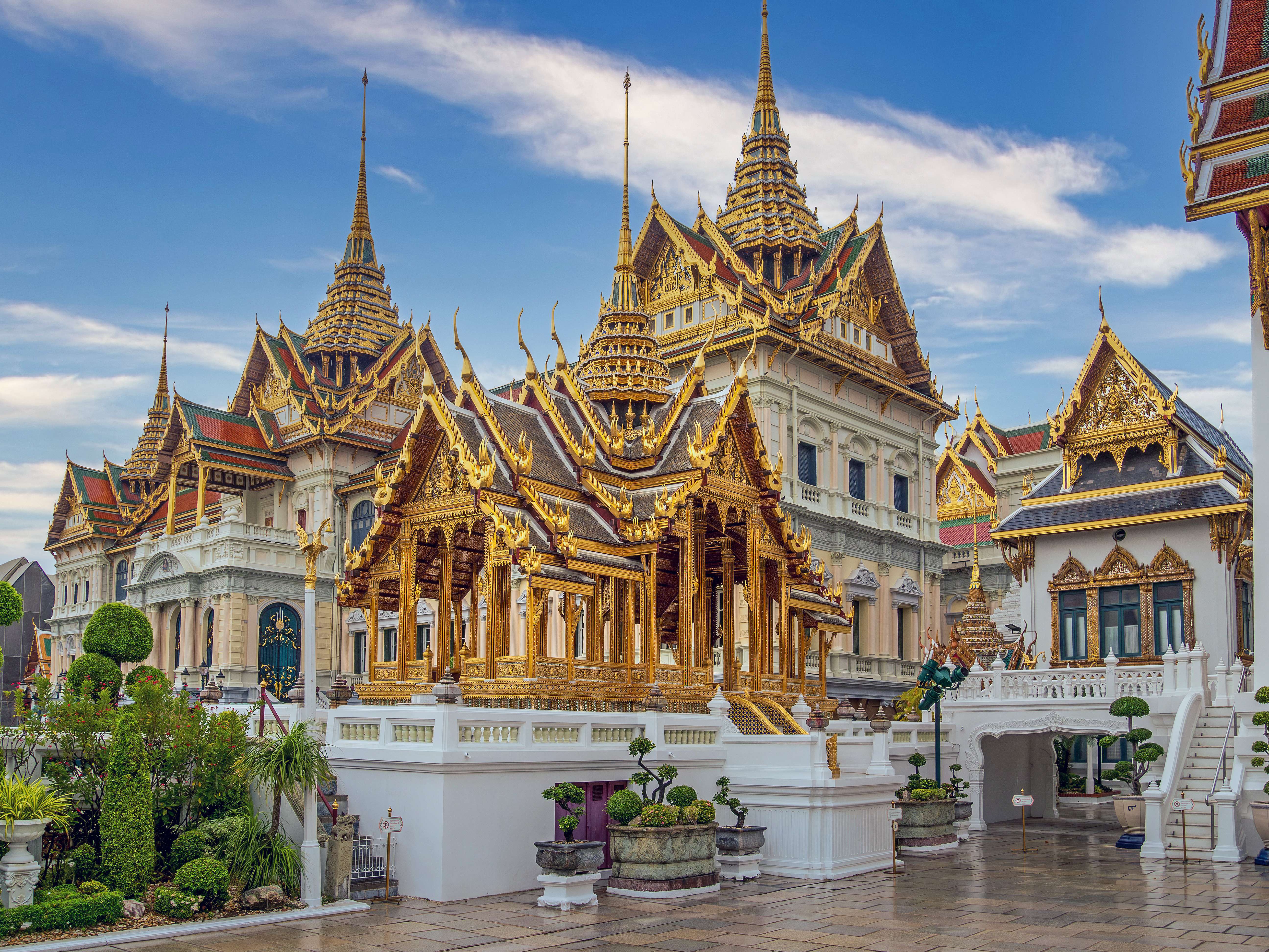 Istana Besar di Bangkok dengan arsitektur emas yang rumit di bawah langit biru.