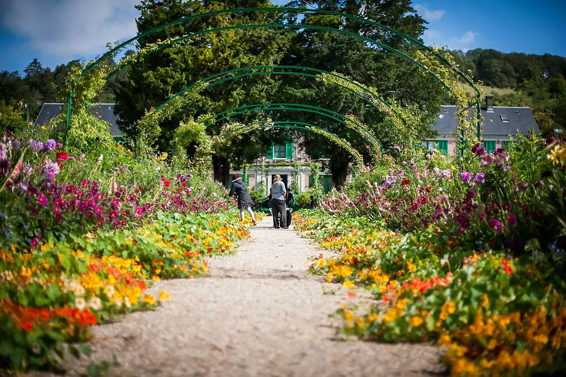 Der Clos Normand in Giverny: blühende Wege in Claude Monets Garten vor seinem rosa Haus mit den grünen Fensterläden, mit Kapuzinerkresse, Iris und Rosen nach der Palette des Malers gepflanzt
