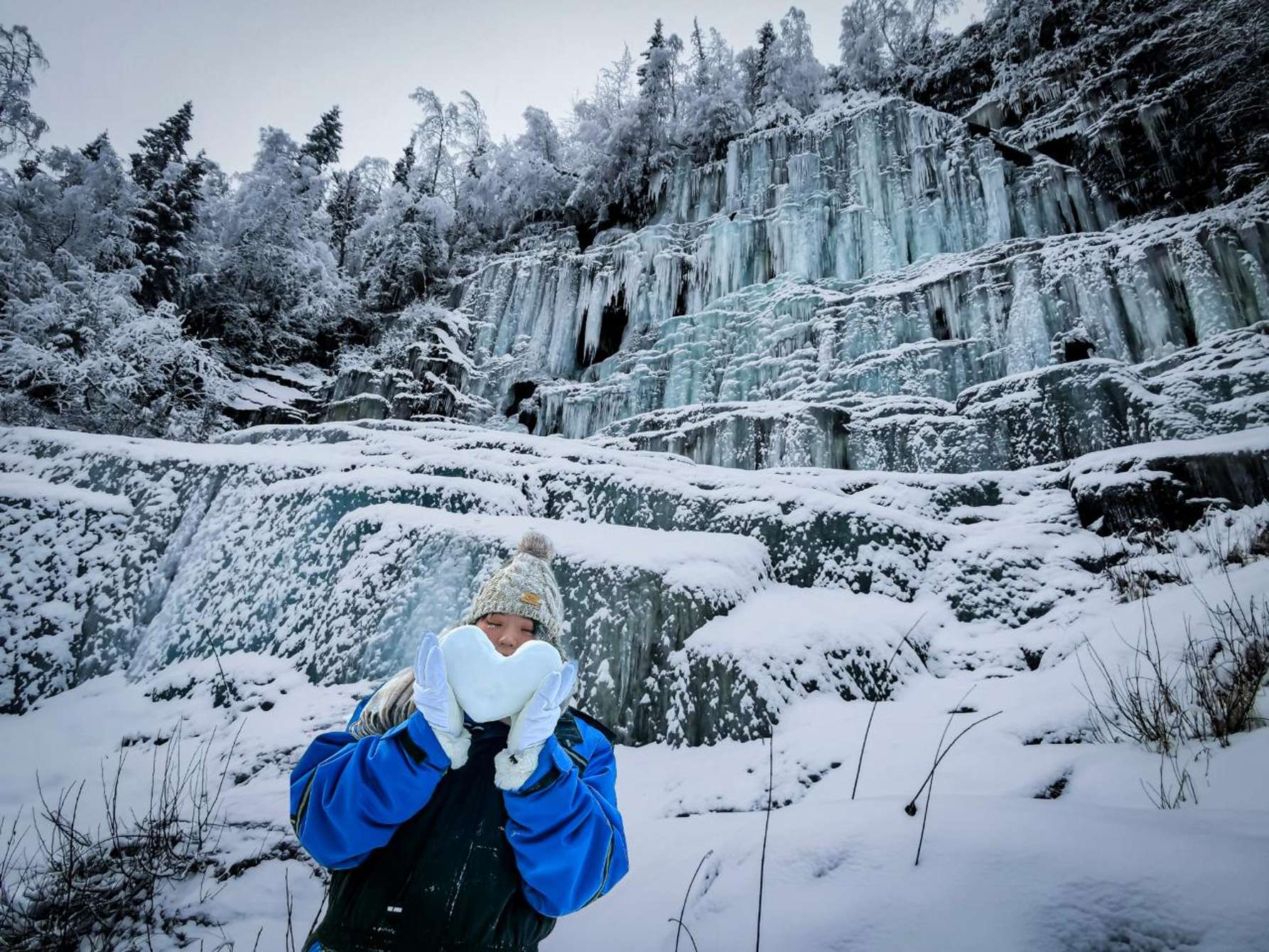 Gefrorene Wasserfälle im Korouoma-Canyon in Finnisch-Lappland: bläuliche Eiswände und riesige Eiszapfen auf dem Grund des verschneiten Canyons, Wanderer am Fuß des erstarrten Wasserfalls