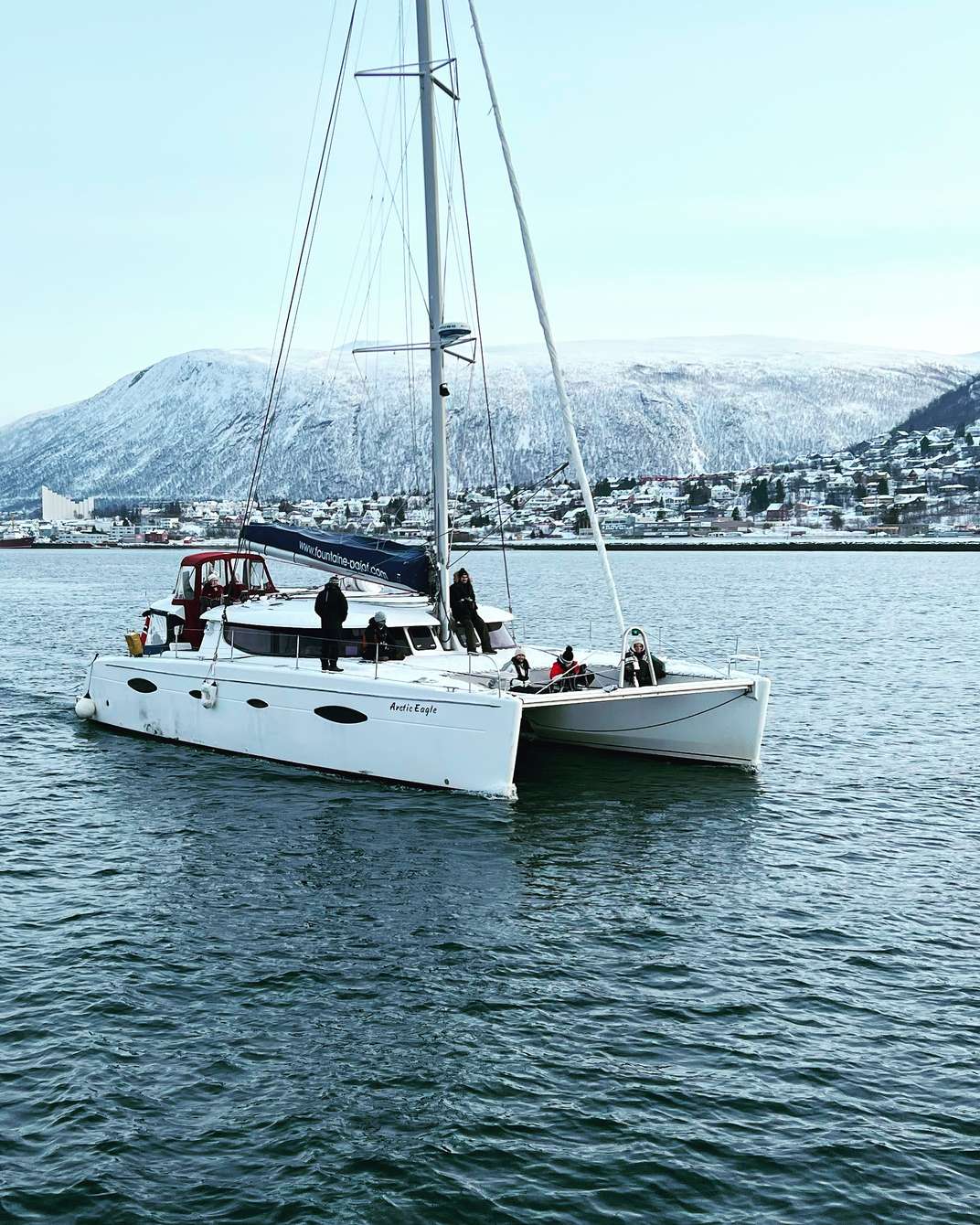 Crucero en catamarán Arctic Eagle por los fiordos de Tromsø: velero de dos cascos navegando entre las montañas árticas nevadas, cubierta exterior y cabina con calefacción para un grupo reducido