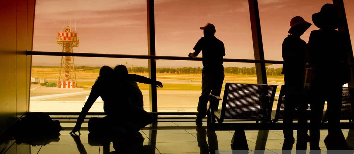 Silhuetas de viajantes e bagagens diante das janelas de um terminal de aeroporto Silhuetas de viajantes e bagagens diante das janelas de um terminal de aeroporto