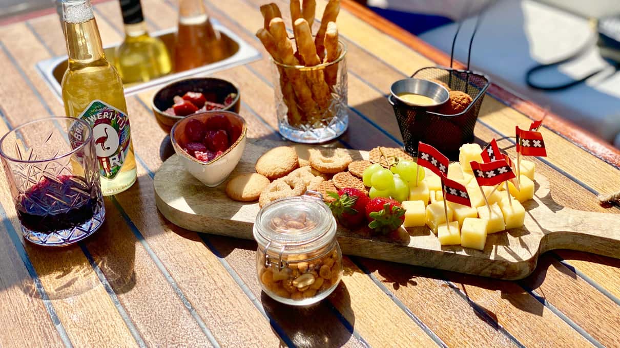 Holzbrett mit Käsewürfeln, Dips, Crackern und Grissini, daneben Gläser mit Wein auf dem Tisch eines Bootes