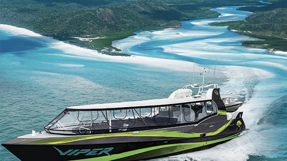 A black and lime green jet speedboat idling in shallow turquoise water at the edge of a white sand beach