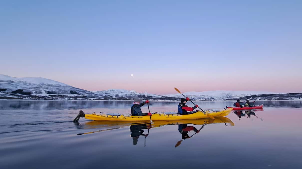 Two yellow double kayaks on a still Tromsø fjord at dusk with the moon over snowy hills
